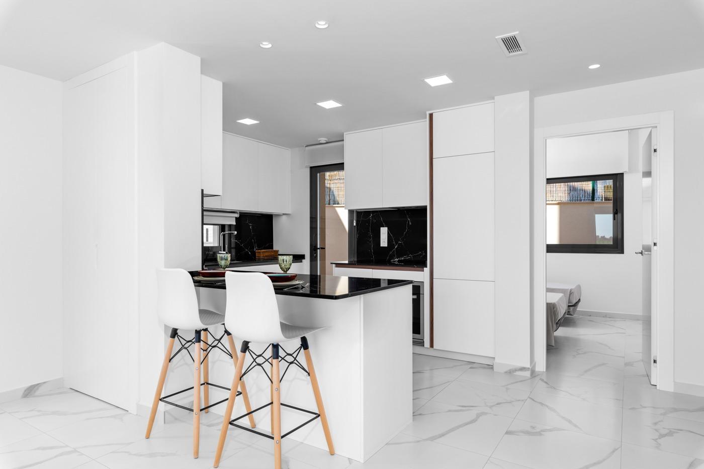Modern white kitchen with a black marble-topped island and four white stools with wooden legs.