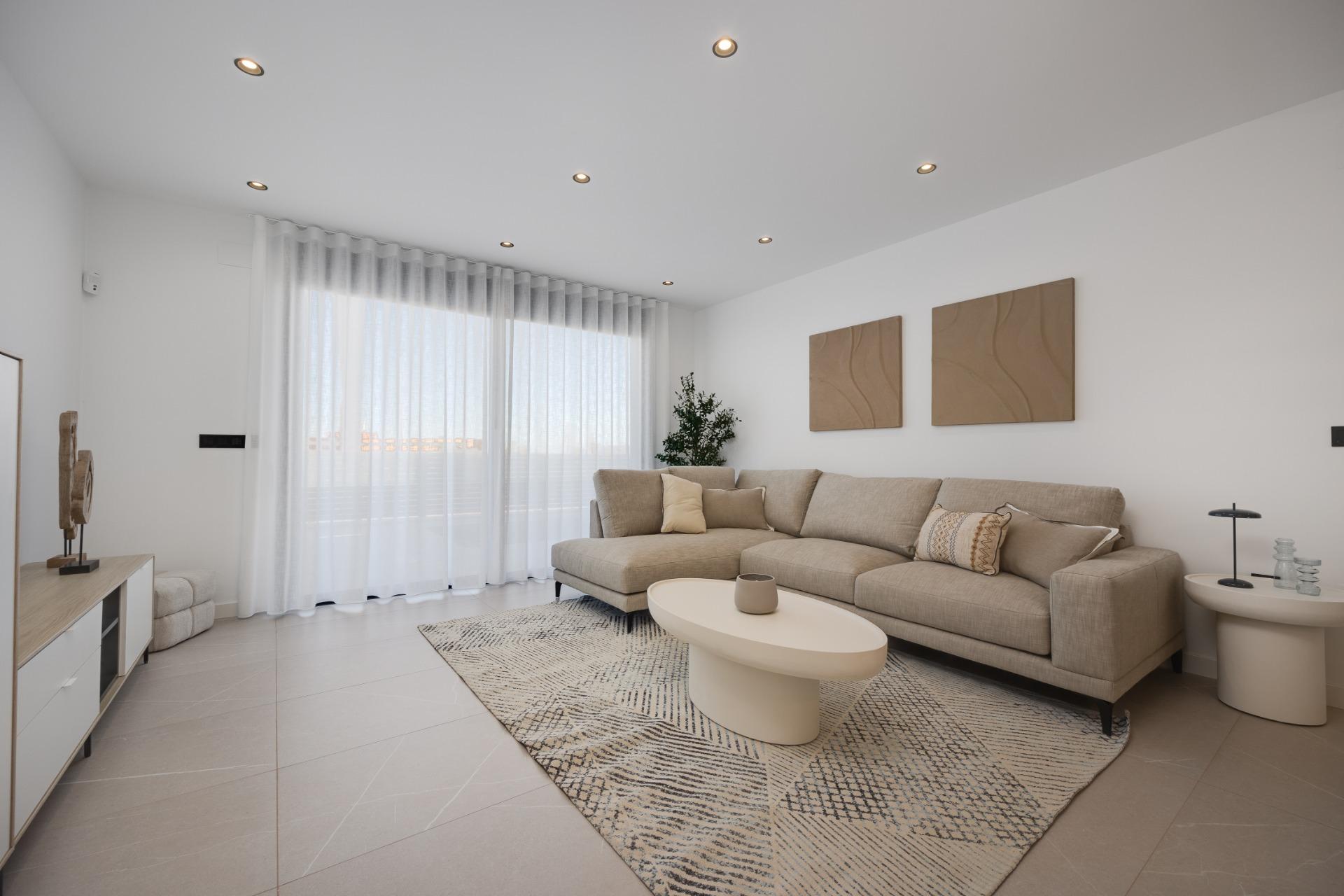 Bright, minimalist living room with a beige sectional, two beige wall art panels, and white sheer curtains over a large window.