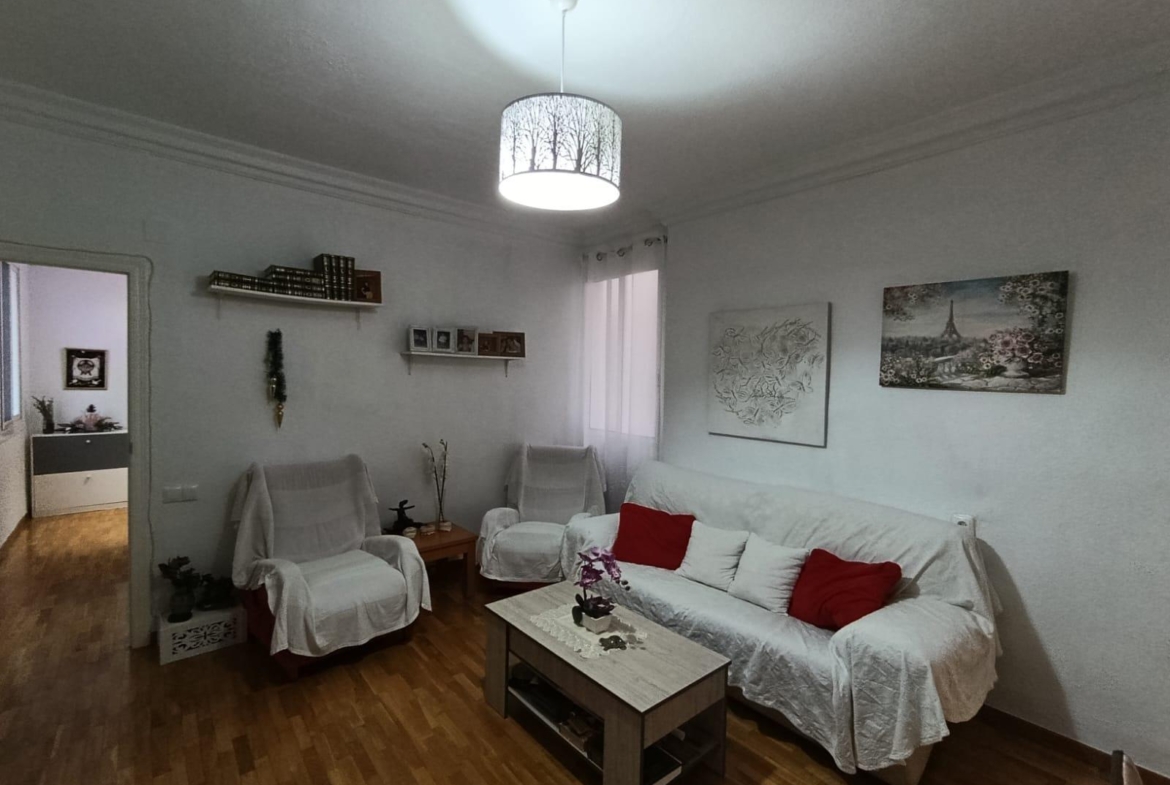 Cozy living room with white sofa and chairs, red cushions, wooden floor, wall art, and a tree-pattern ceiling lamp.