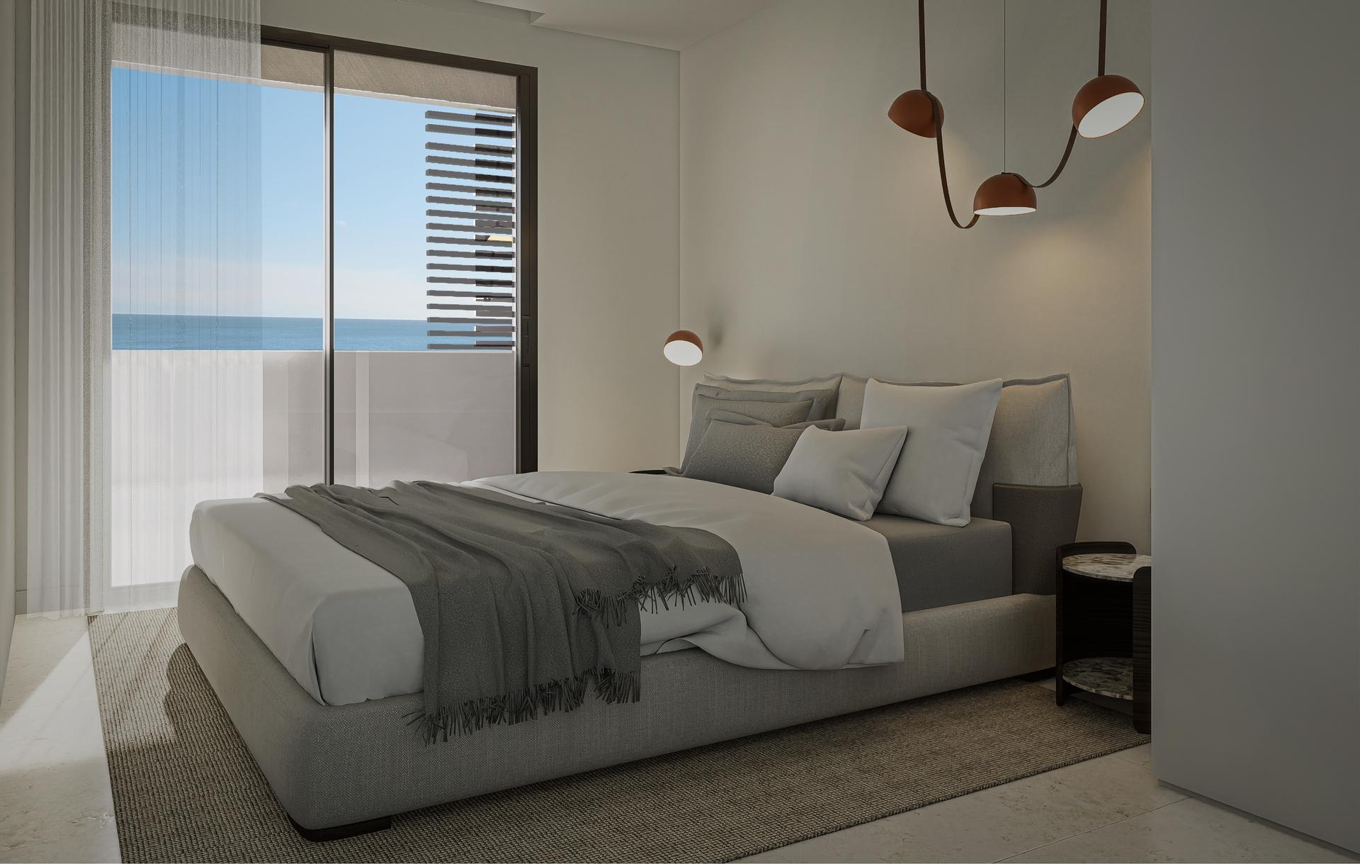 Hotel-style bedroom with a king bed, white sheets and gray throw, overlooking the ocean through a glass balcony door.