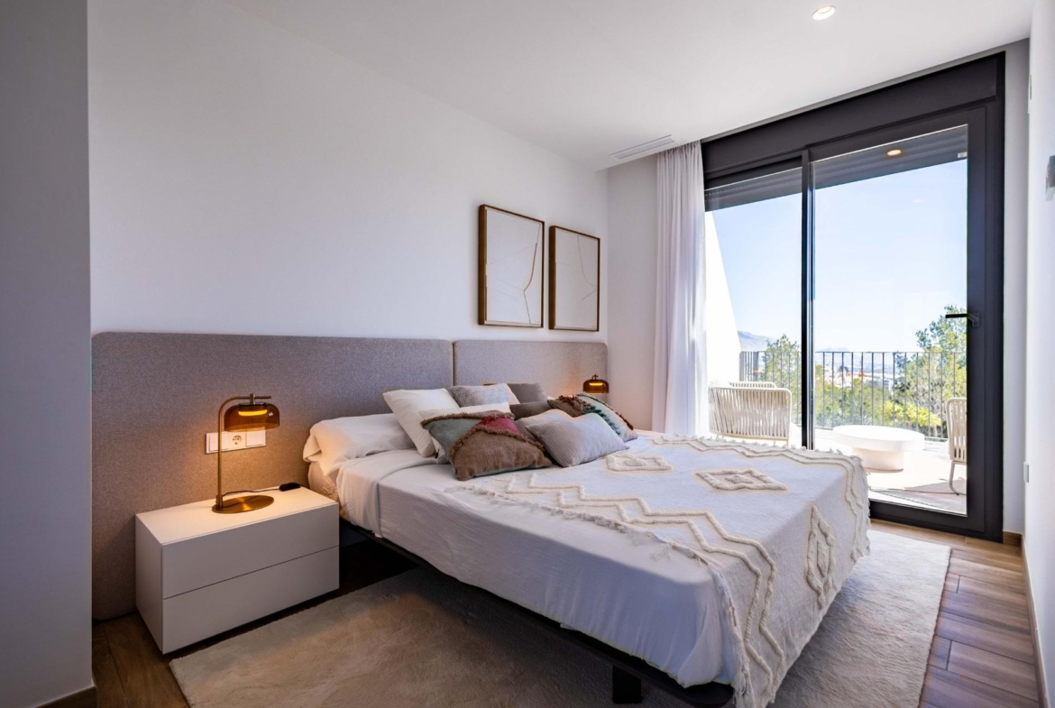Bright hotel-style bedroom with a low upholstered headboard, white bedding, two framed abstract artworks, a white nightstand, and a warm amber bedside lamp on each side of the bed with soft lighting.