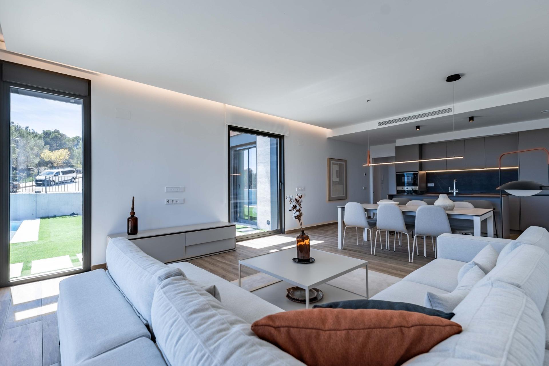 Bright, modern open-plan living and dining area with large glass doors to the outside and a sleek kitchen in the background.