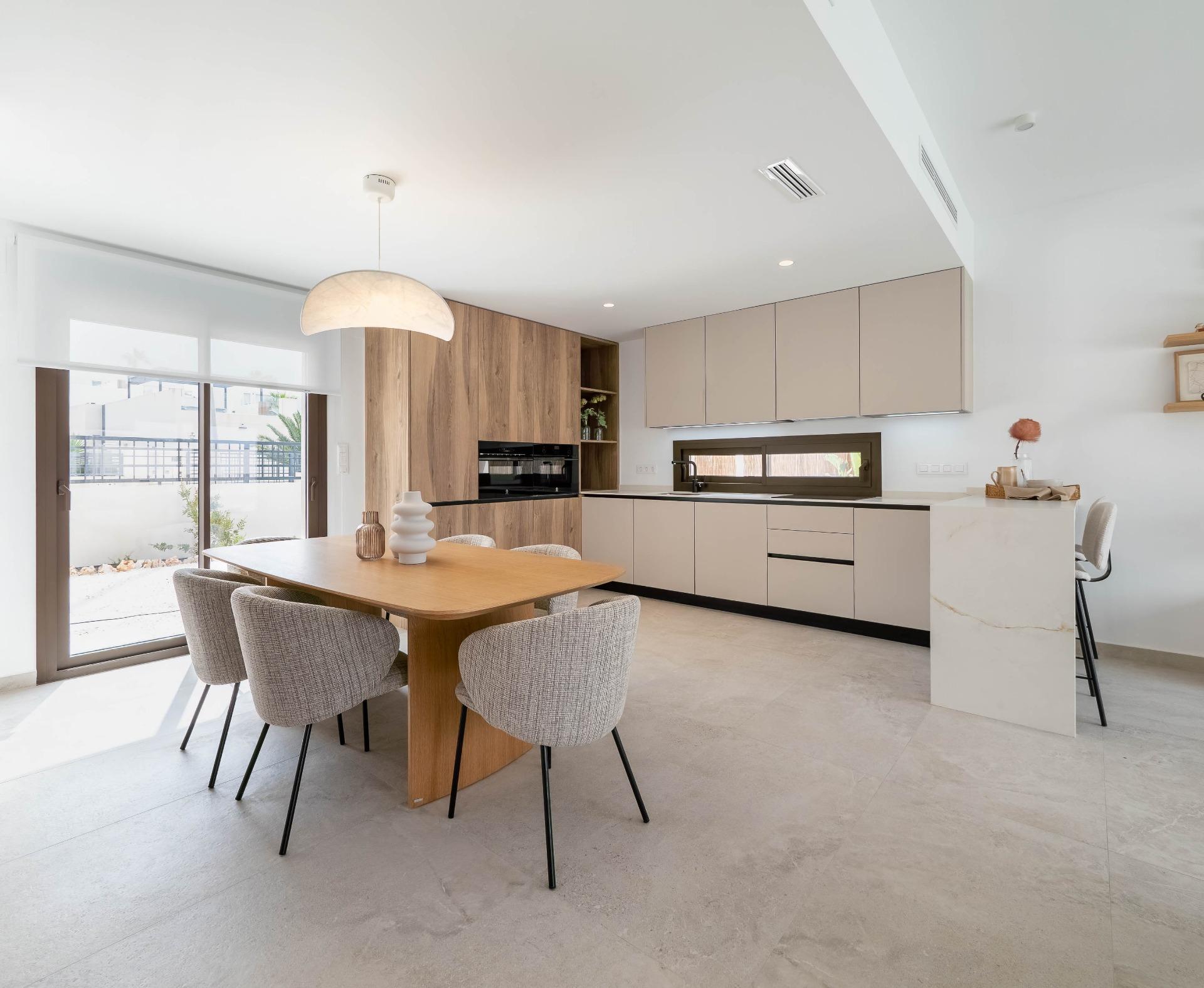 Bright modern kitchen and dining area with beige cabinetry, light wood table, and gray upholstered chairs.