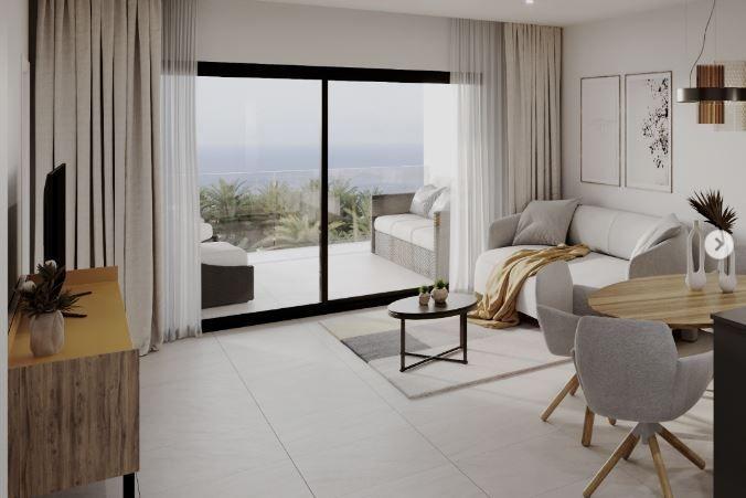Bright living room with a sofa and dining area, sliding glass doors open to a balcony with an ocean view above the horizon.