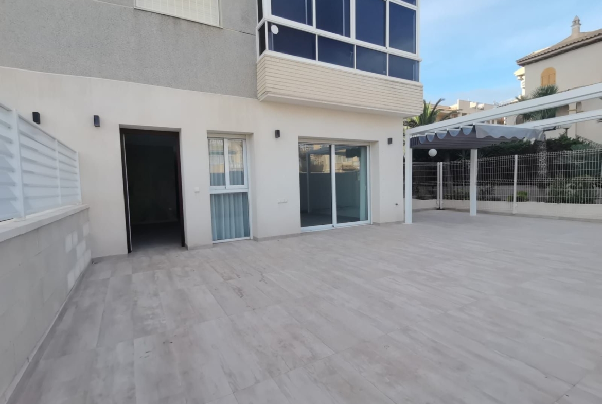 Wide tiled patio outside a modern white building with sliding glass doors and a covered outdoor area.