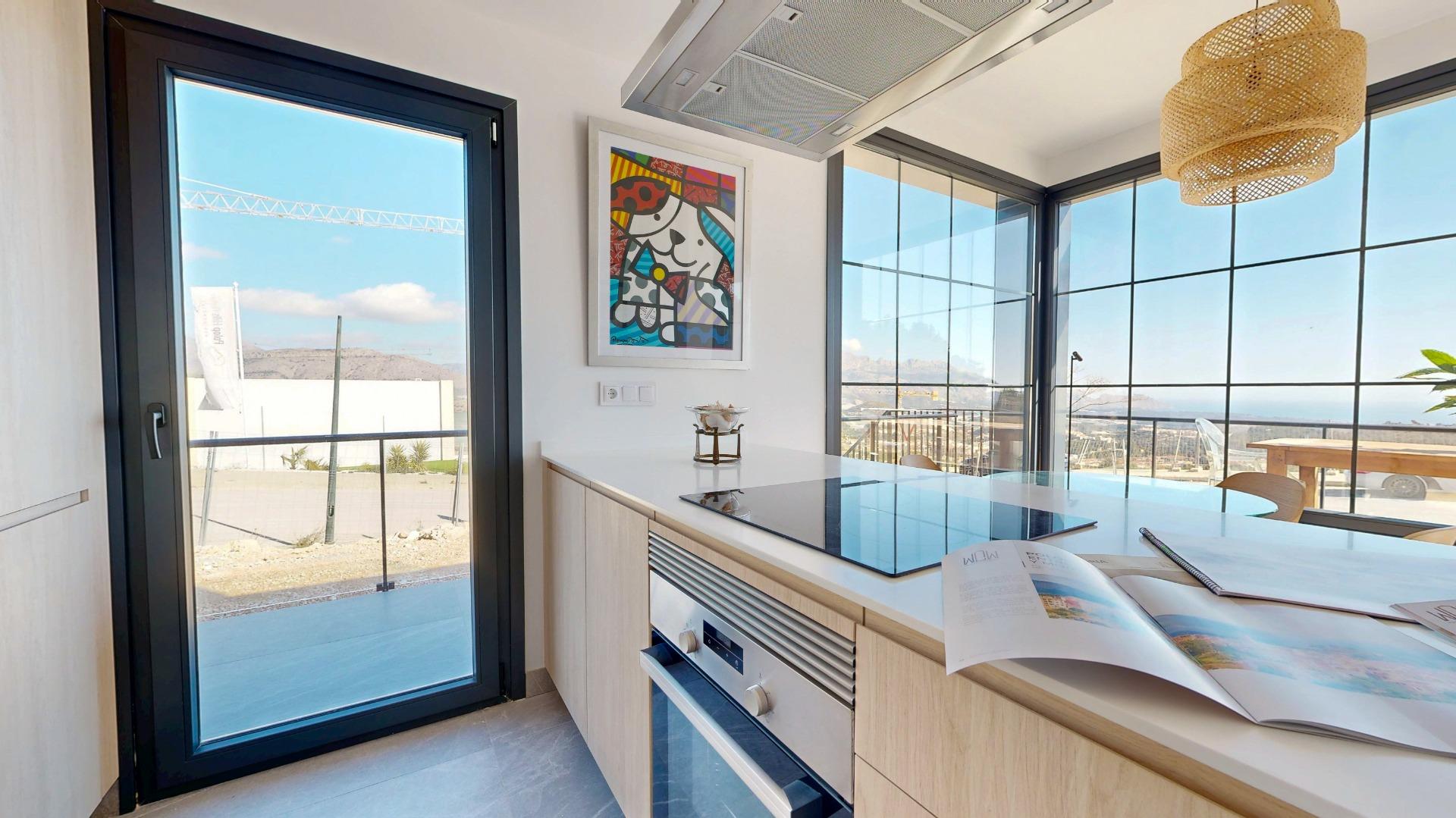 Modern kitchen with light wood cabinets, a glass induction cooktop on an island, and large windows showing a scenic outdoor view.