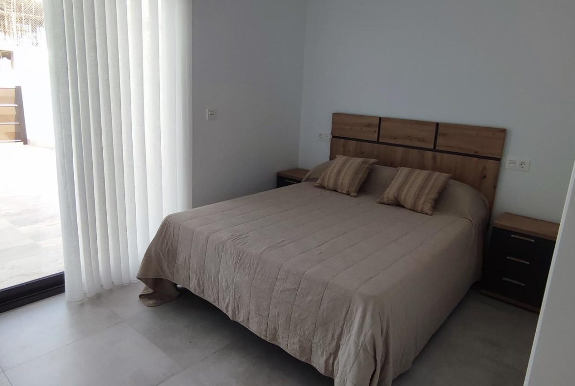 Bedroom with a double bed, beige bedding, three pillows, and wooden headboard flanked by two matching nightstands.