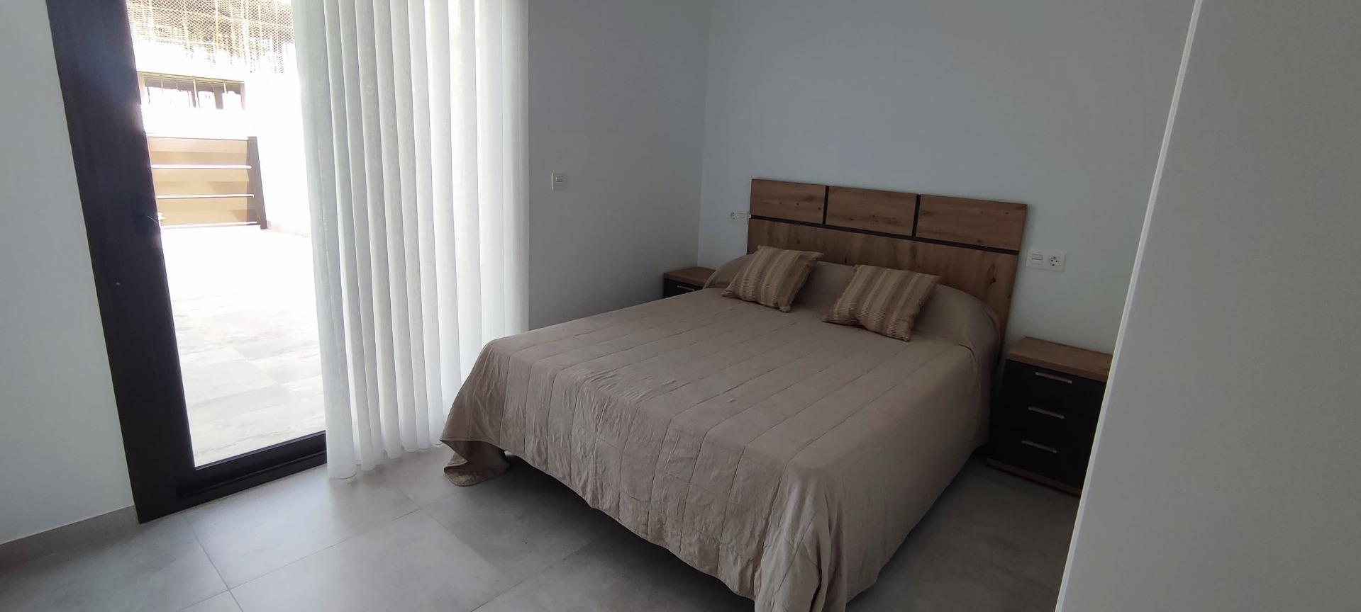 Bedroom with a double bed, beige bedding, three pillows, and wooden headboard flanked by two matching nightstands.