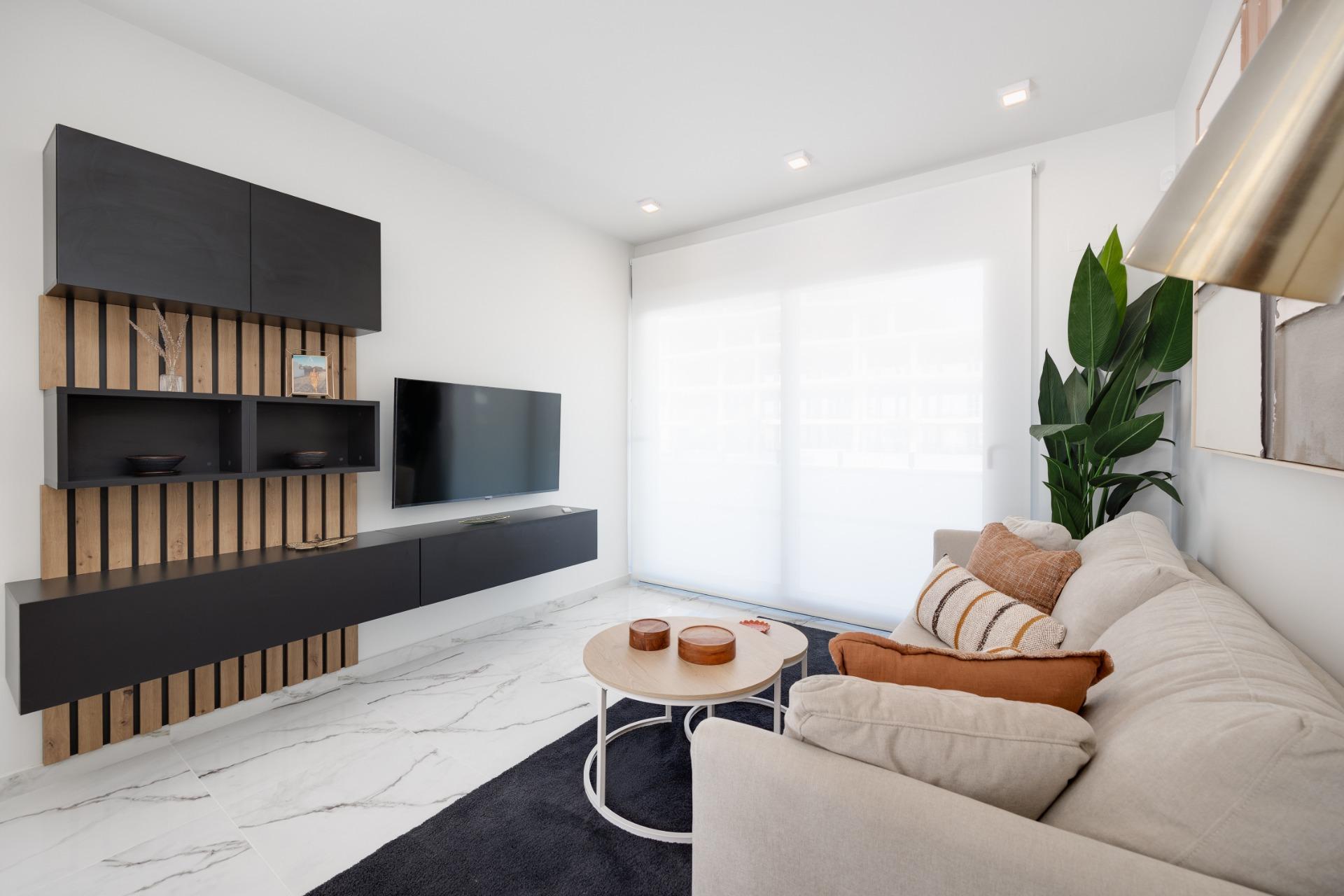 Contemporary living room with a dark wall-mounted media unit, TV, and a beige sectional sofa by a large window.