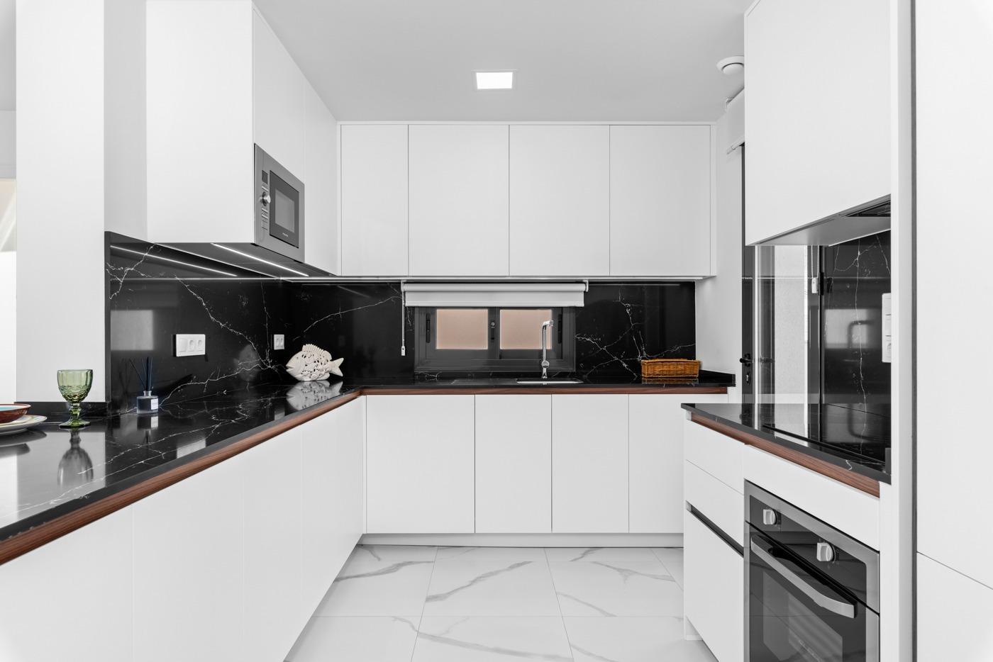 Modern white L-shaped kitchen with black marble countertops and built-in stainless steel appliances.