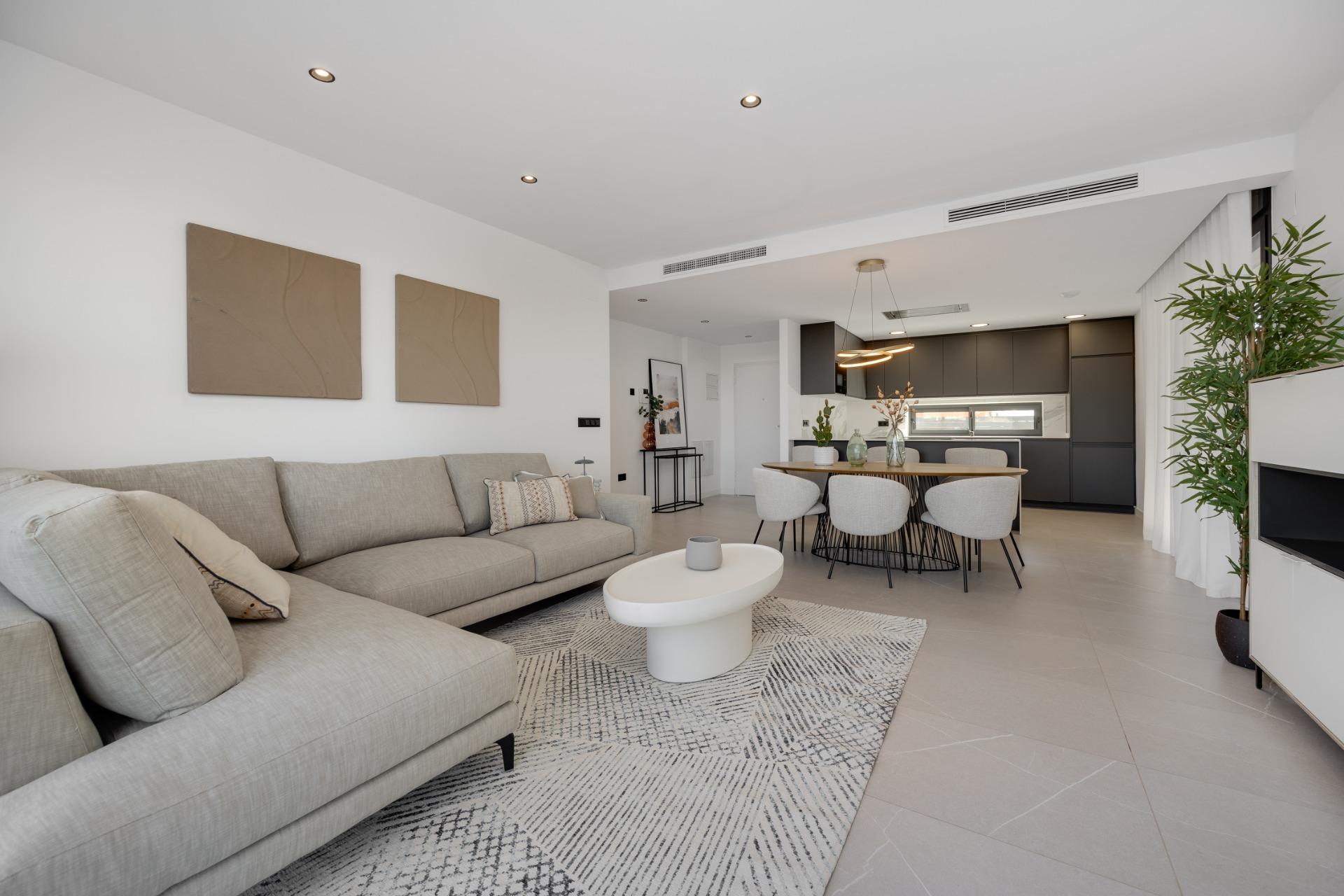 Open-plan living room with a beige sectional sofa, white walls, and a modern dining area near the kitchen.