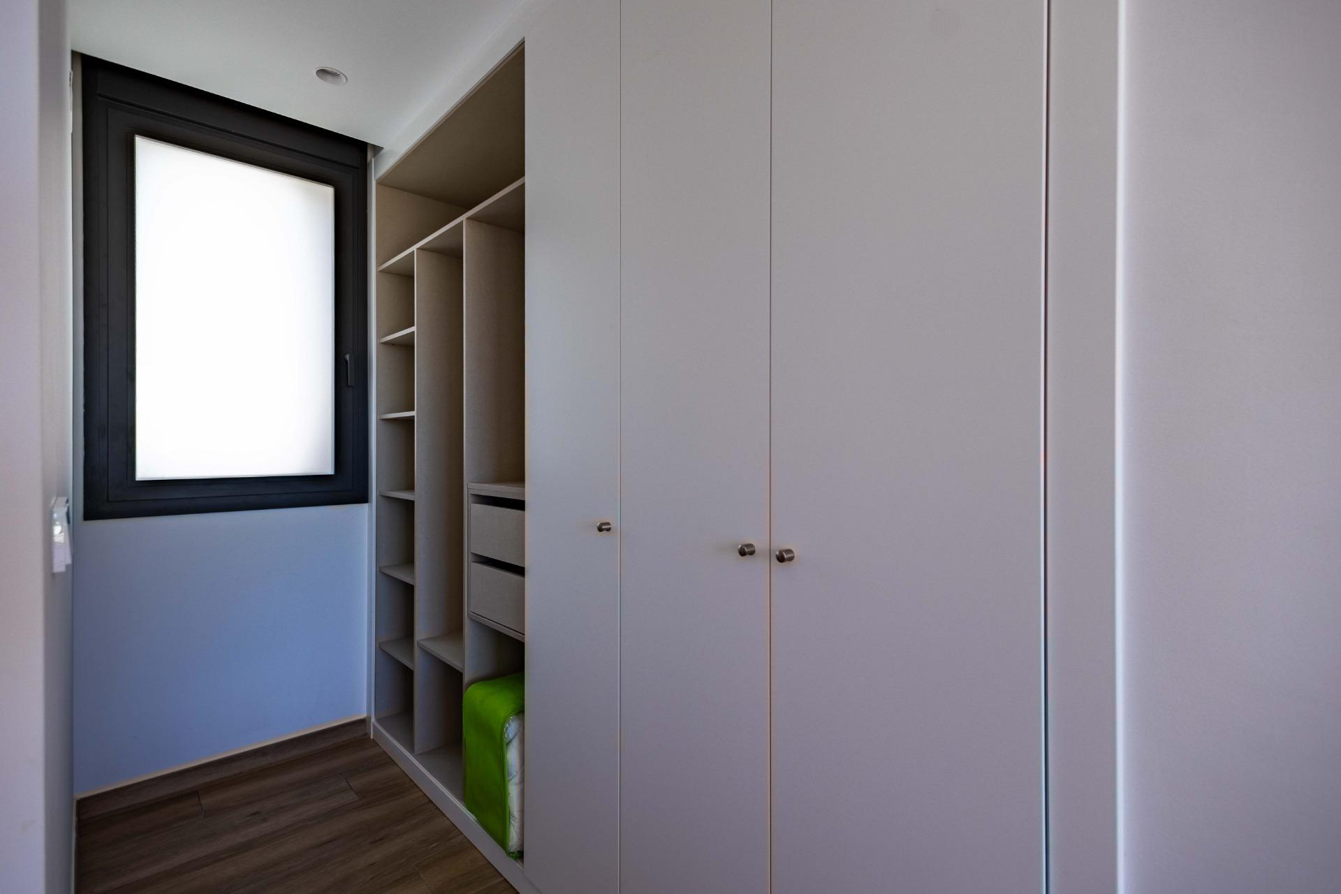 Walk-in closet with white built-in cabinets, open shelving, and a frosted window at the end of the room.