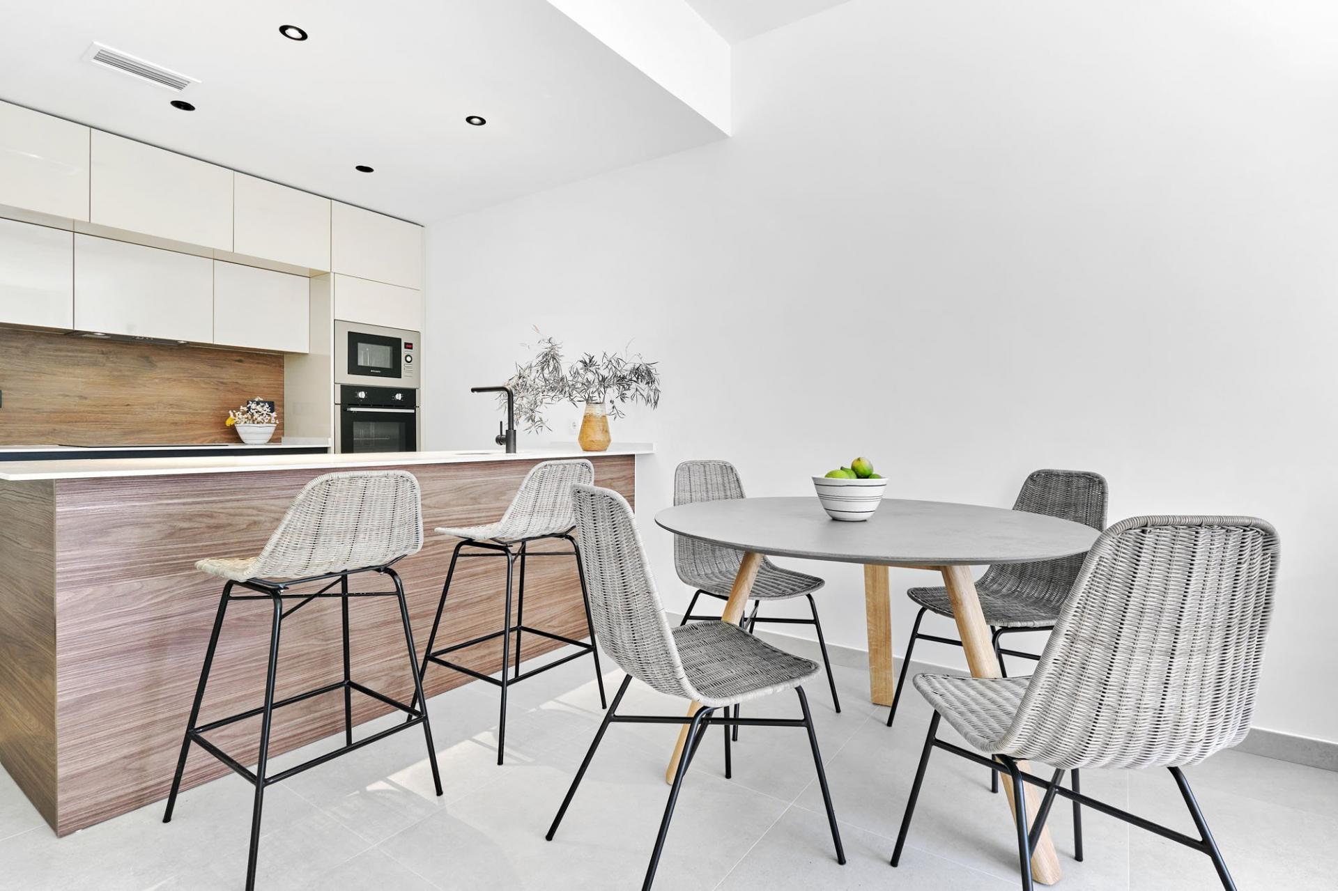 Modern kitchen with white cabinets, wood island, and a round gray dining table surrounded by woven chairs.