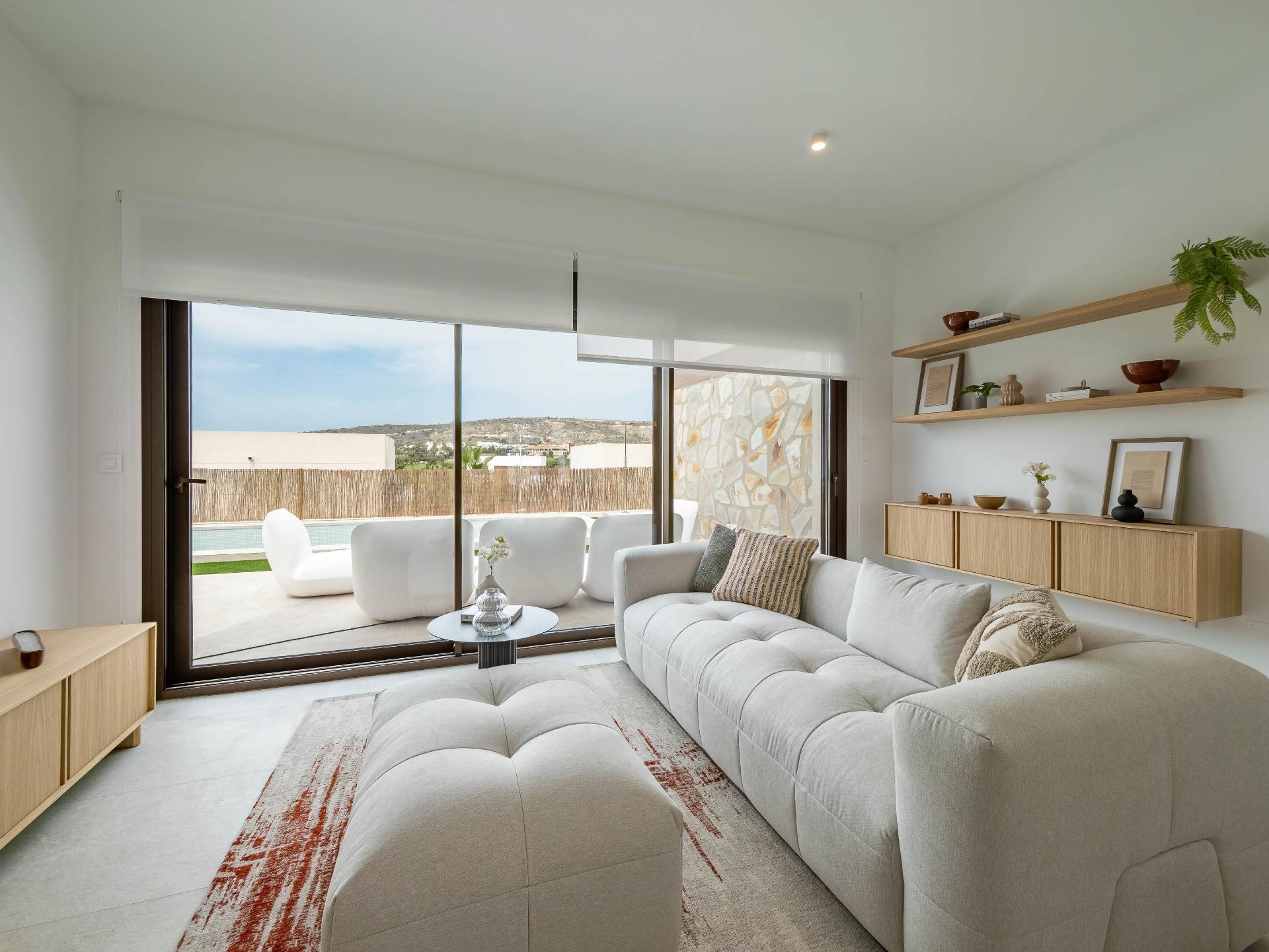 Bright living room with a gray sectional, wooden shelves, and large sliding glass doors opening to an outdoor patio.