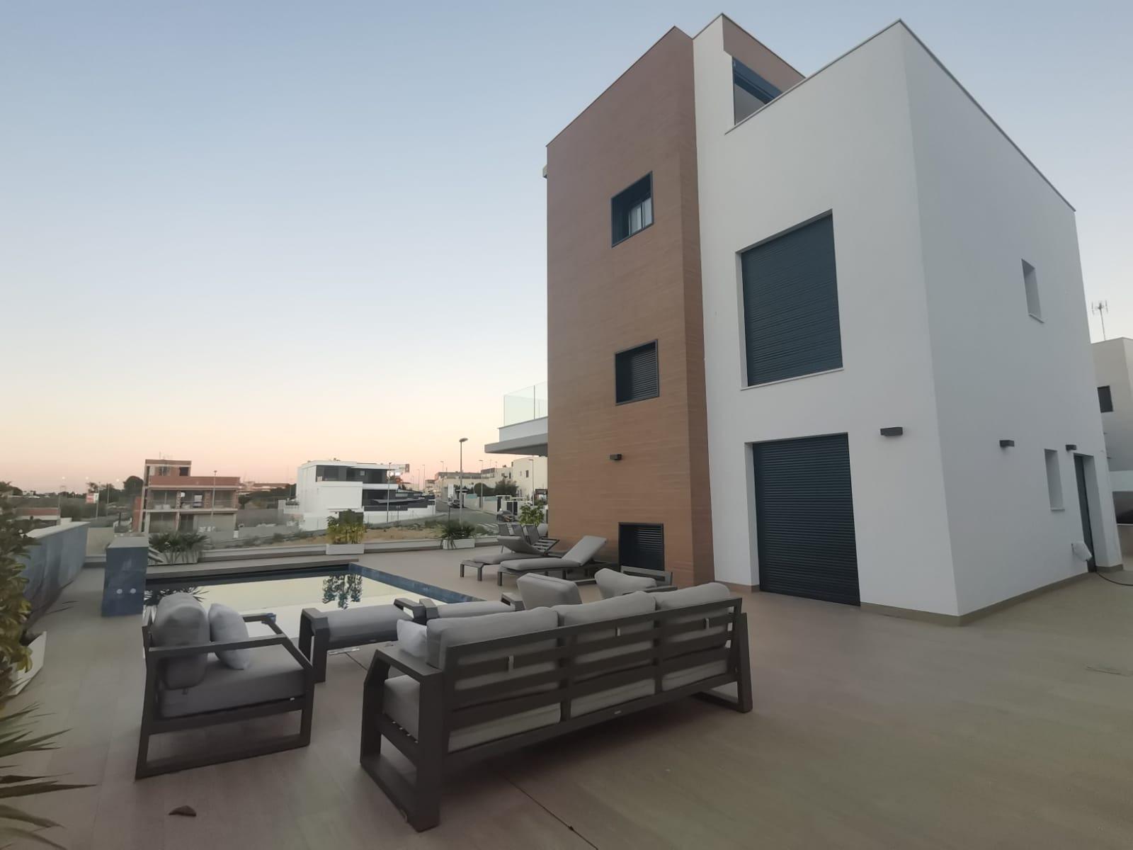 Modern white and brown villa with a pool deck and outdoor seating at dusk.