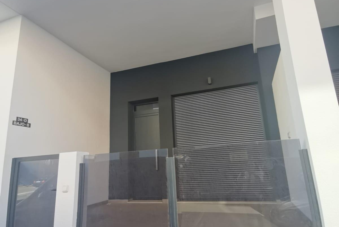 Modern building entrance with glass railing, dark gray walls, and a metal roll-up door.