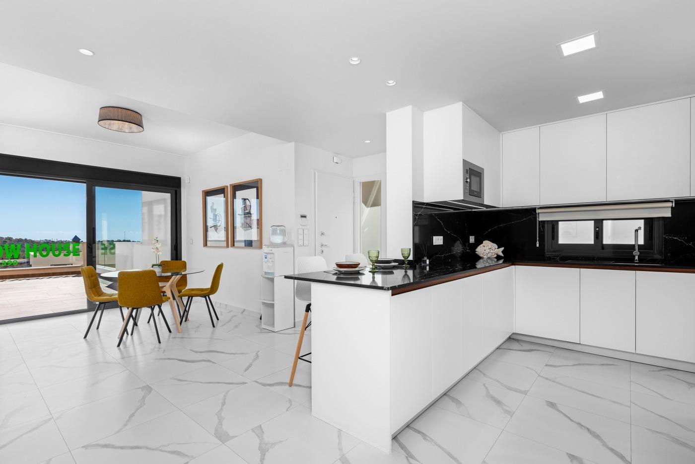 Open-plan kitchen and dining area with white cabinets, black marble backsplash, and a central island; mustard chairs around a glass table by a large sliding door to the outdoors