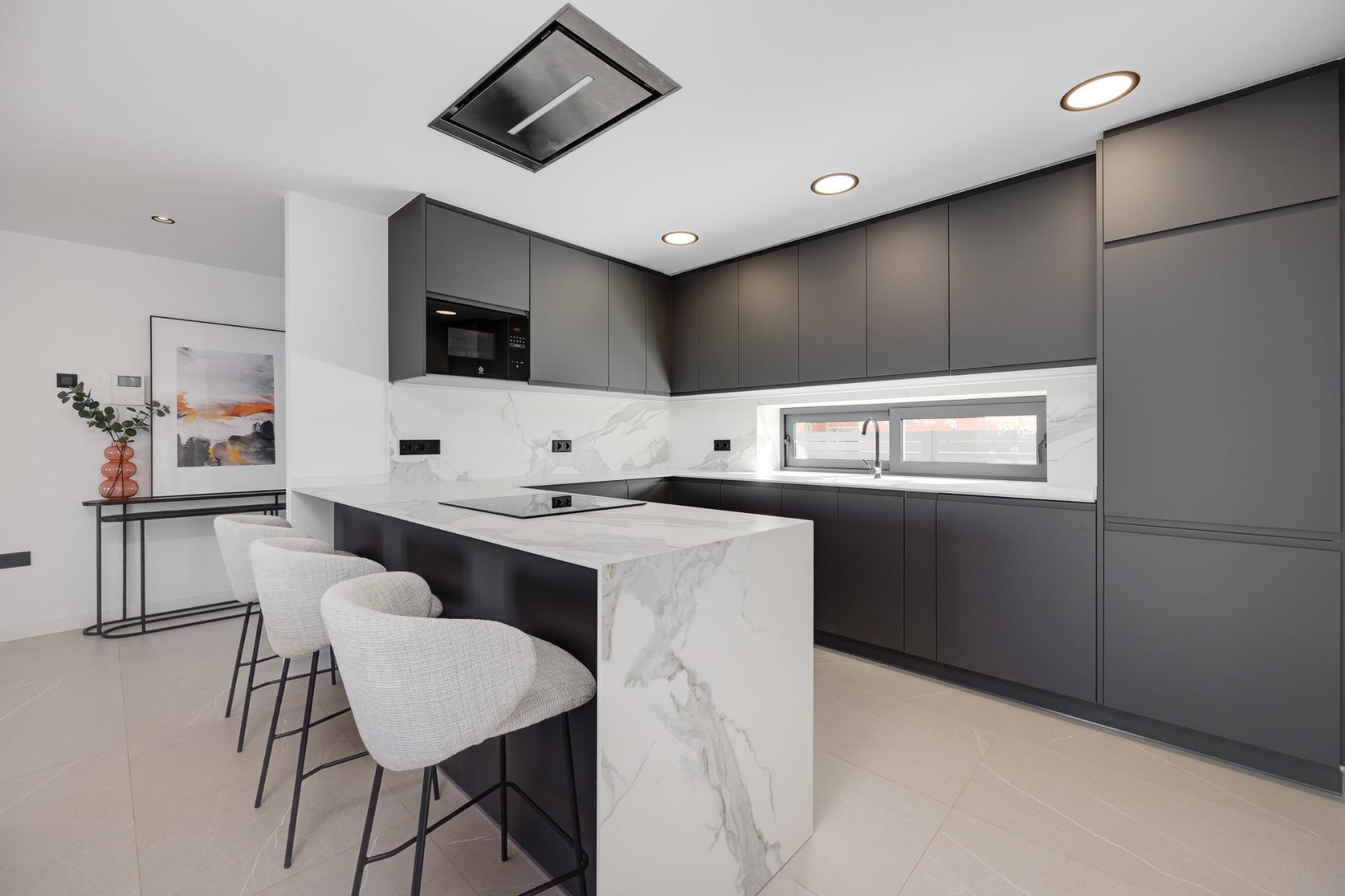 Modern kitchen with dark gray cabinets, marble island, and bar seating along a light floor and white walls