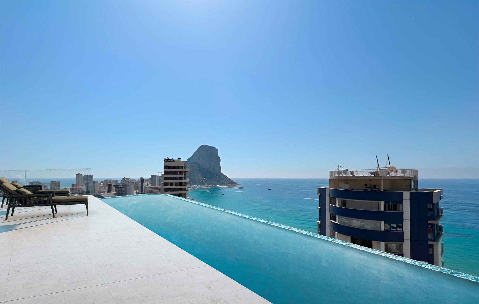 Rooftop pool terrace with white tiles and lounge chairs, overlooking the blue sea and distant rocky island.