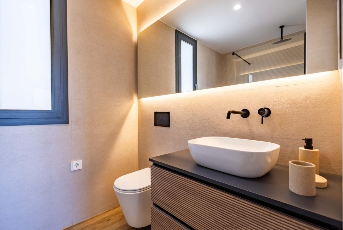 Modern bathroom with beige tile walls, wall-mounted faucet, and white vessel sink on a dark wooden vanity
