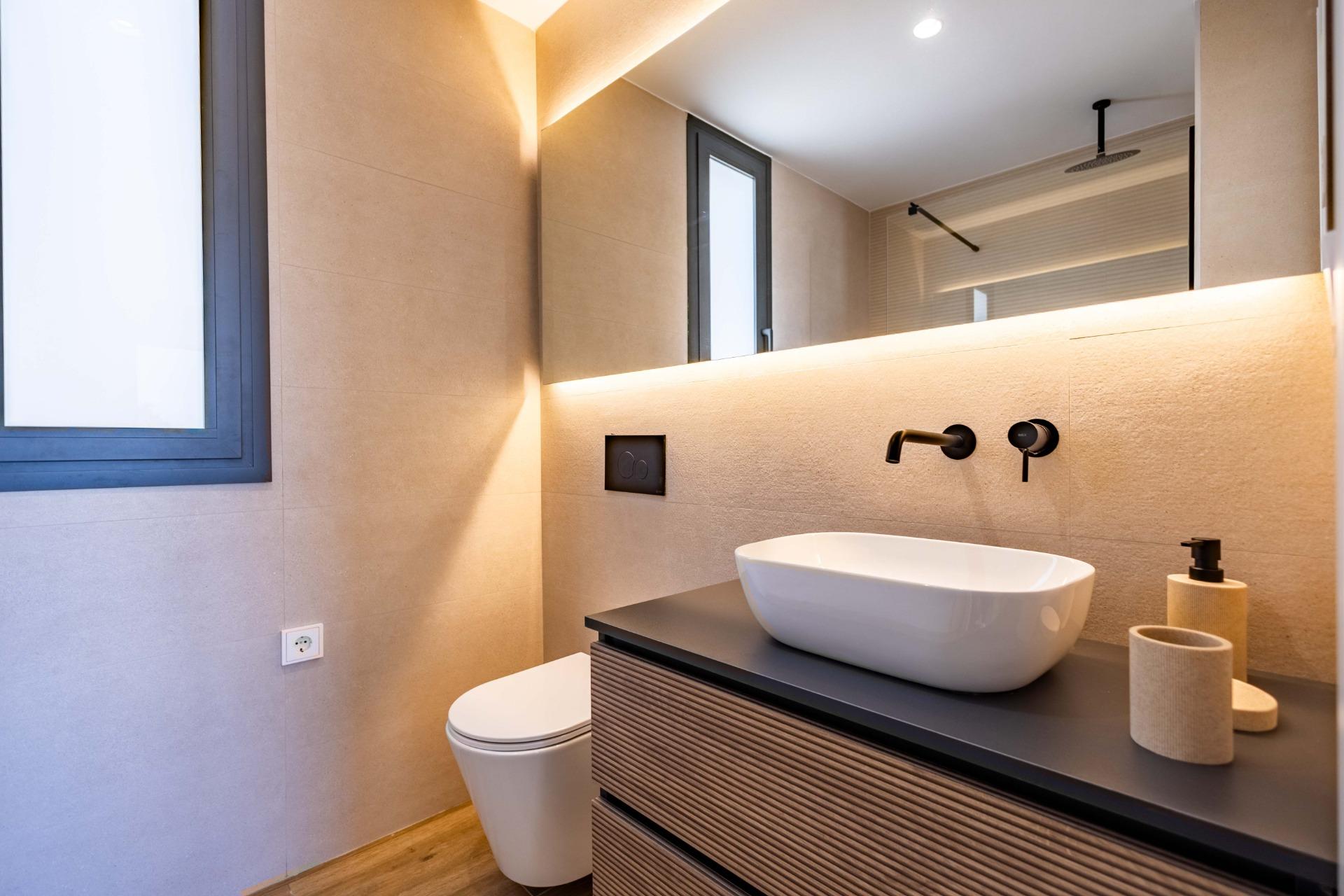 Modern bathroom with beige tile walls, wall-mounted faucet, and white vessel sink on a dark wooden vanity