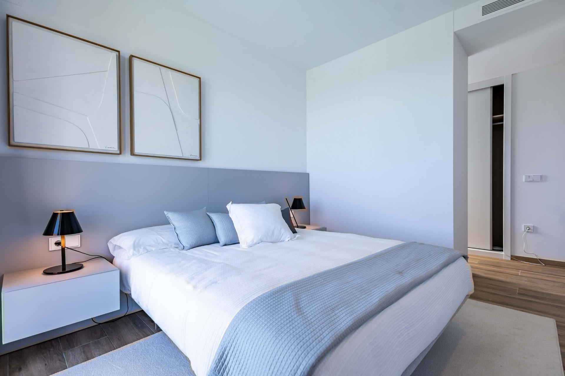 Modern hotel-style bedroom with a large bed, gray headboard, white-blue bedding, two nightstands, and black lamps.