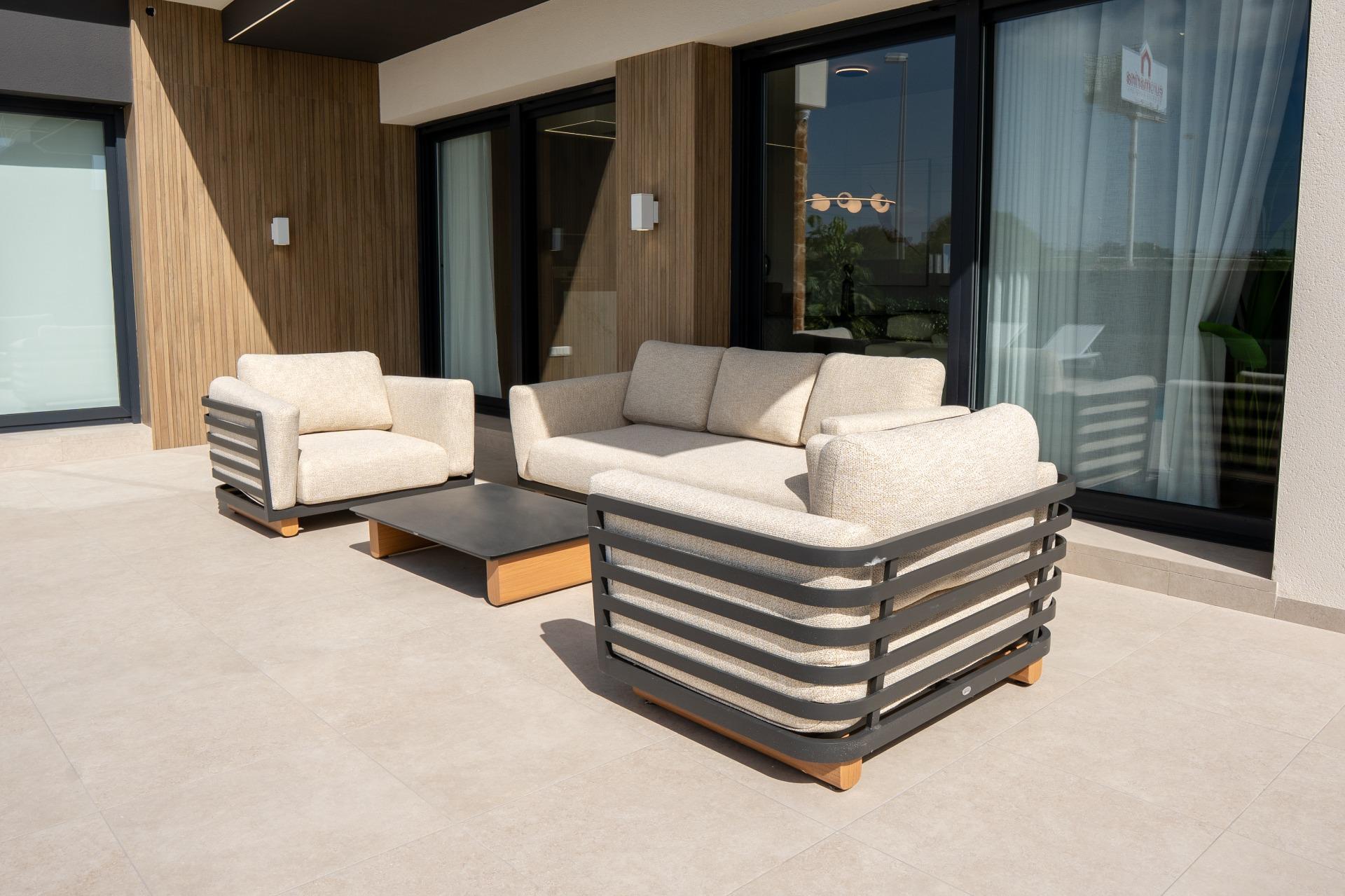 Outdoor patio with beige cushioned seating and a coffee table against a wooden wall and glass doors.