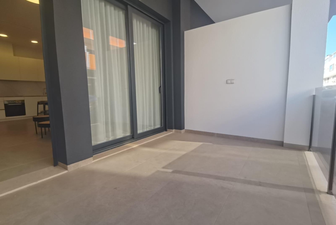 Outdoor balcony with sliding glass doors to a modern kitchen; grey walls and light tile flooring in a contemporary space.
