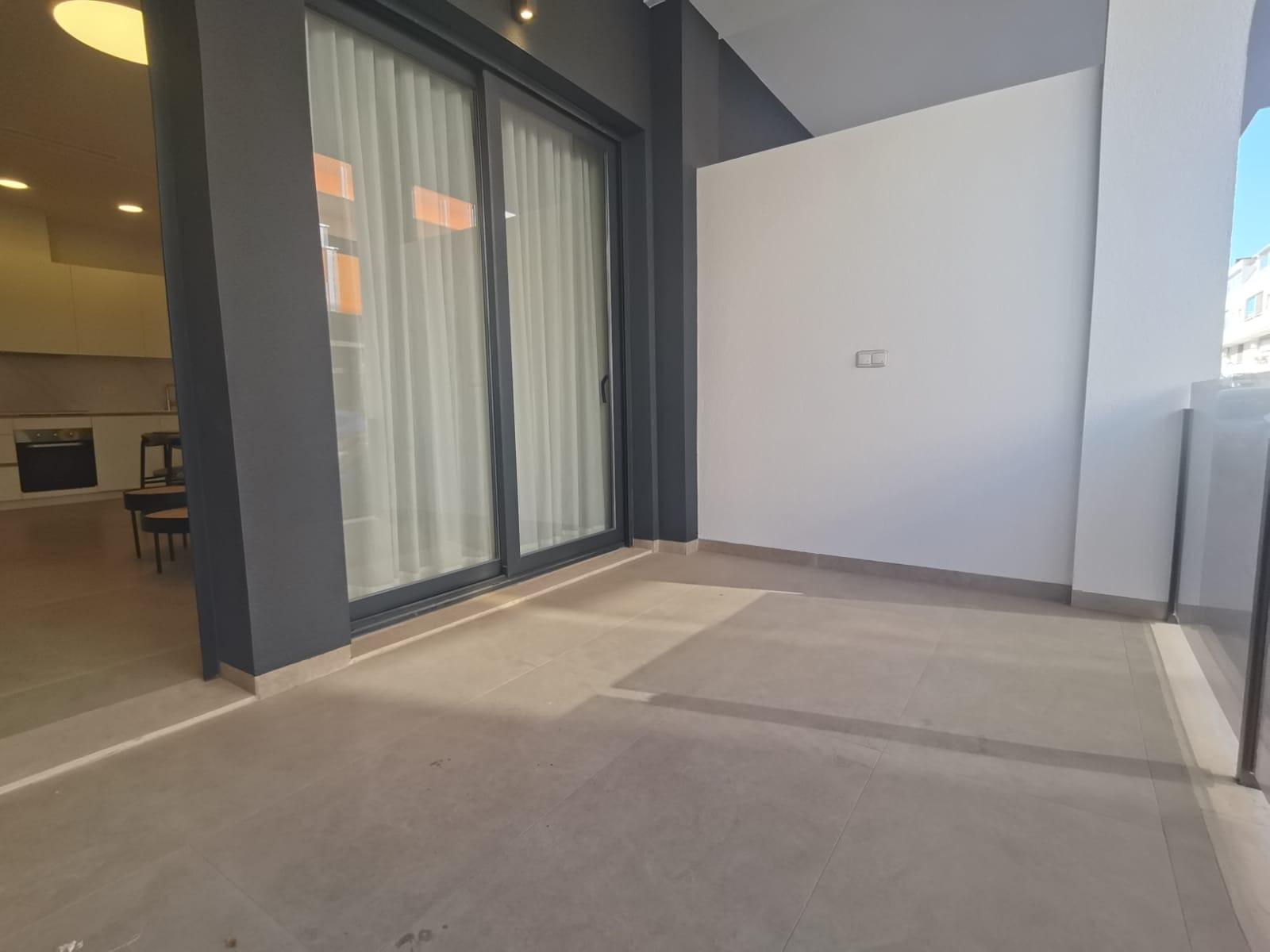 Outdoor balcony with sliding glass doors to a modern kitchen; grey walls and light tile flooring in a contemporary space.
