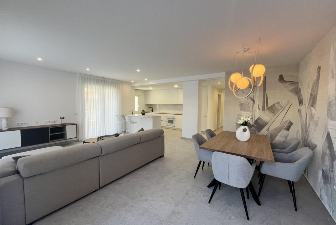 Open-plan living and dining room with a grey sectional sofa, wooden dining table, leaf-wall mural, and warm pendant lights.