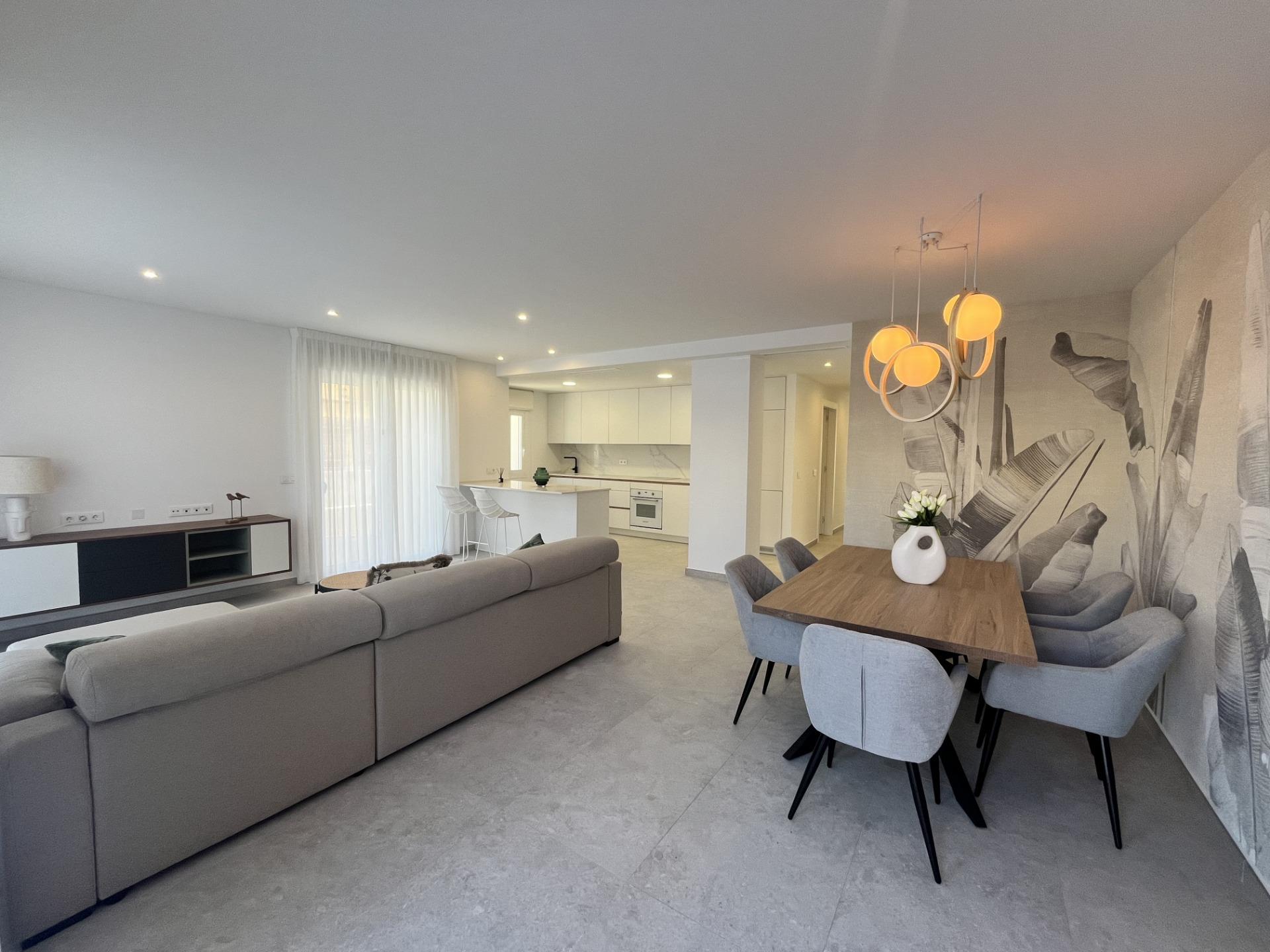 Open-plan living and dining room with a grey sectional sofa, wooden dining table, leaf-wall mural, and warm pendant lights.