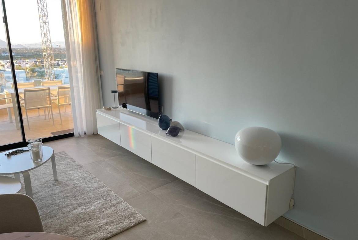 Modern living room with a low white media console, TV, and a large round white lamp along a pale blue wall; glass balcony doors on the left.