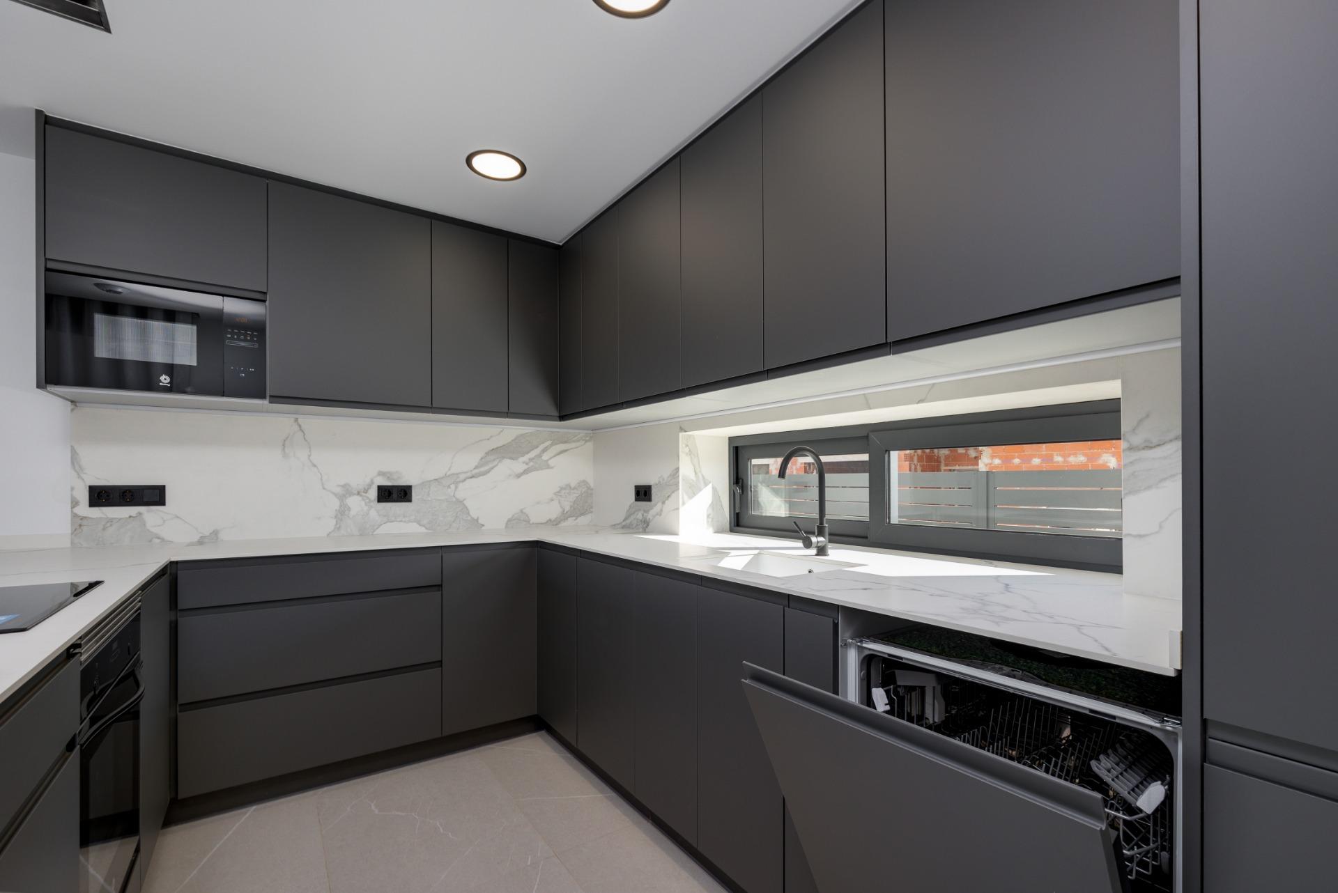 Modern L-shaped kitchen with dark gray cabinets, marble backsplash, and built-in appliances including a microwave and an open dishwasher under a windowed counter.