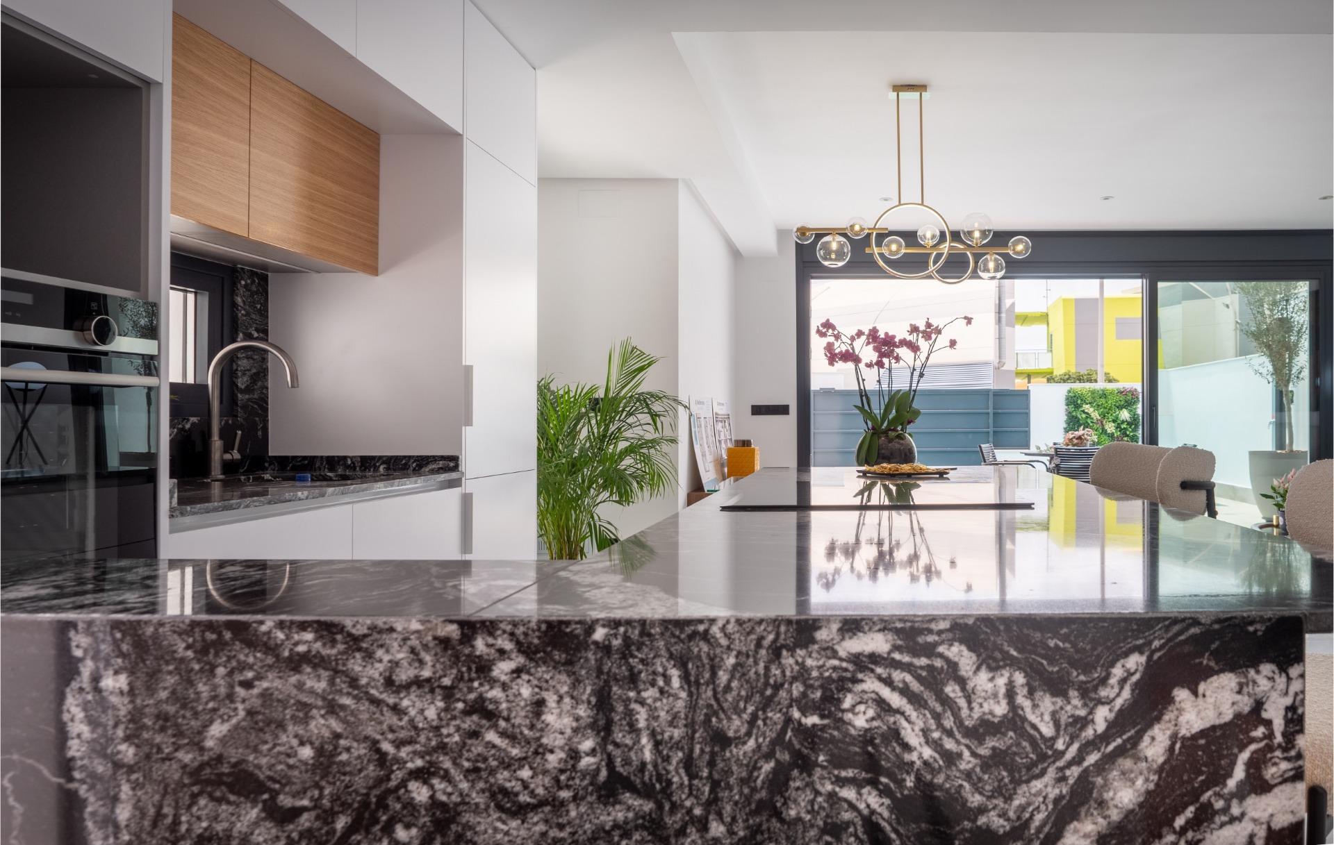 Modern kitchen interior with a black marble island, white cabinets, and a gold circular chandelier over the island.