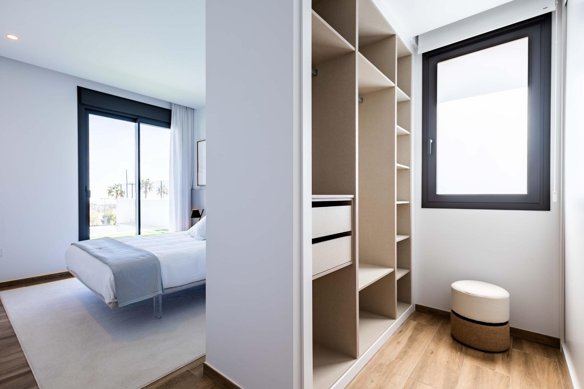 Bright modern bedroom with a large sliding glass door to a balcony, view of palm trees outside, and a white bed with light gray bedding partially visible behind a partition.