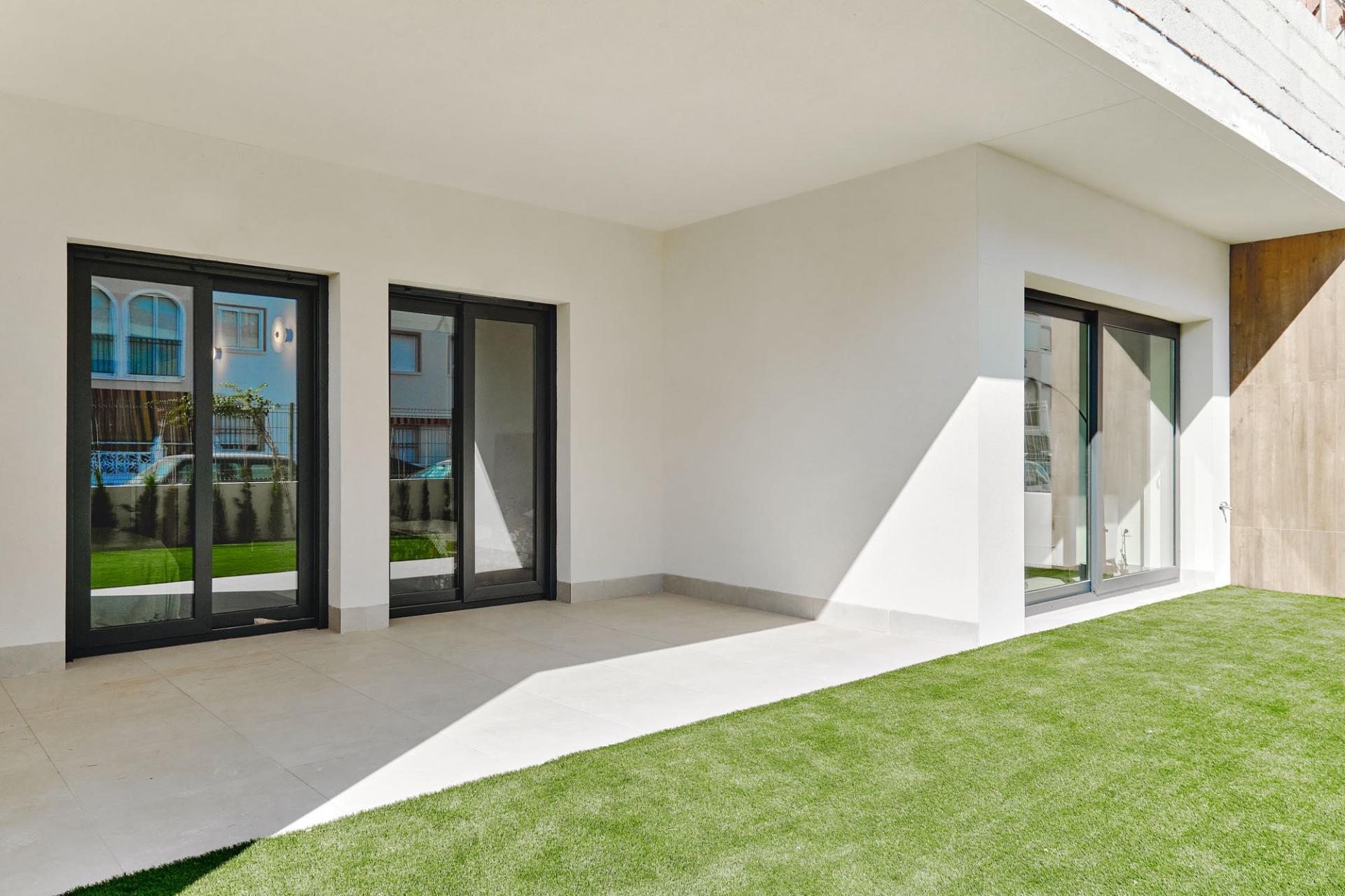 Modern white courtyard with large black-framed sliding glass doors opening to a tiled patio and green lawn.
