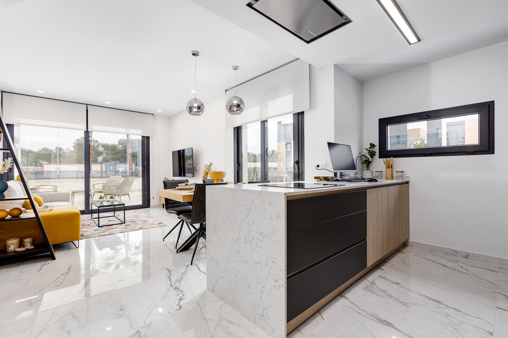 Open-plan living area with marble floors, kitchen island, and large glass doors to a balcony; yellow sofa, coffee table, and wall-mounted TV.