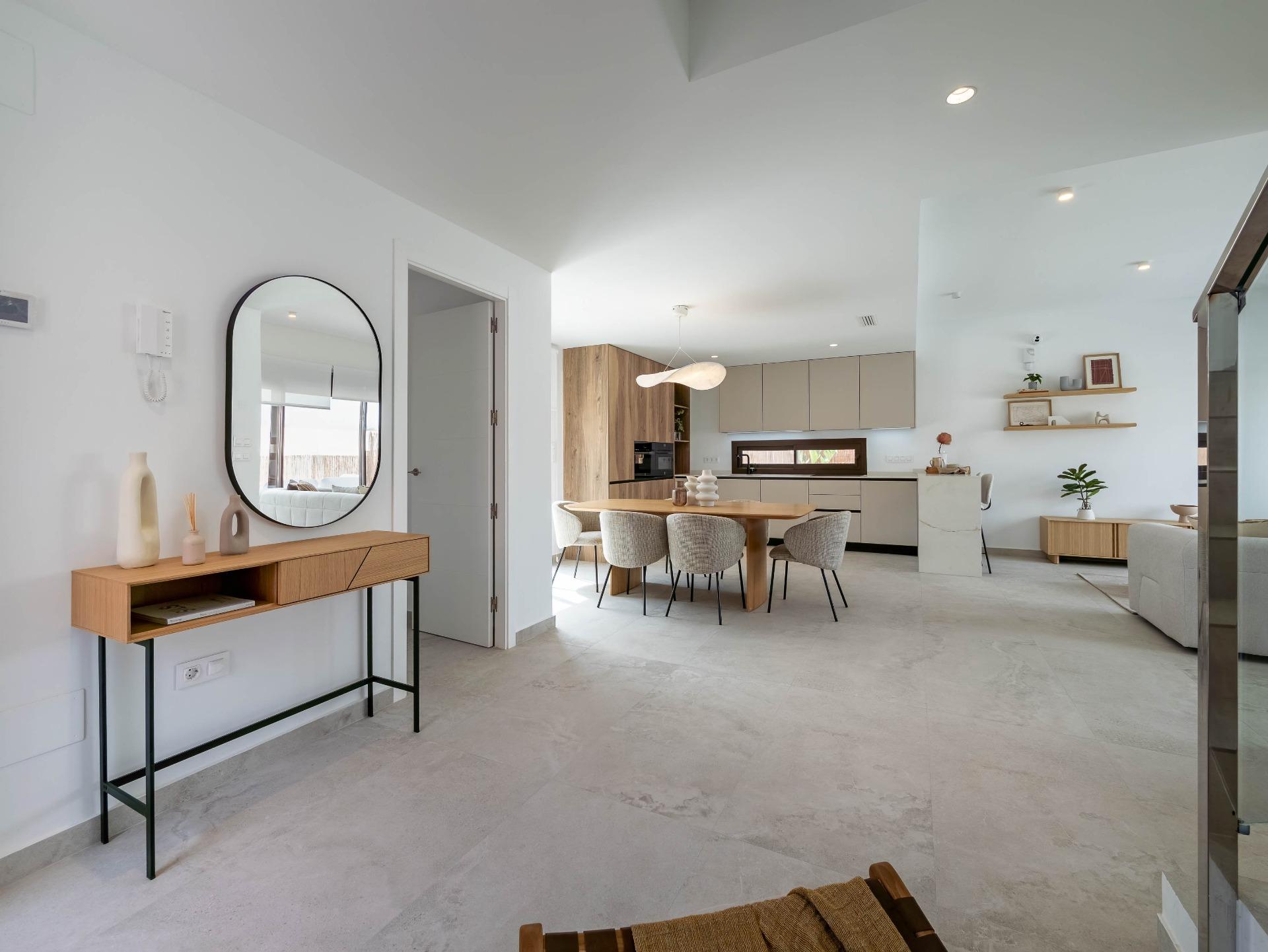 Open-plan kitchen and dining area with beige cabinets, wooden dining table, and six gray upholstered chairs under a sculptural pendant light.