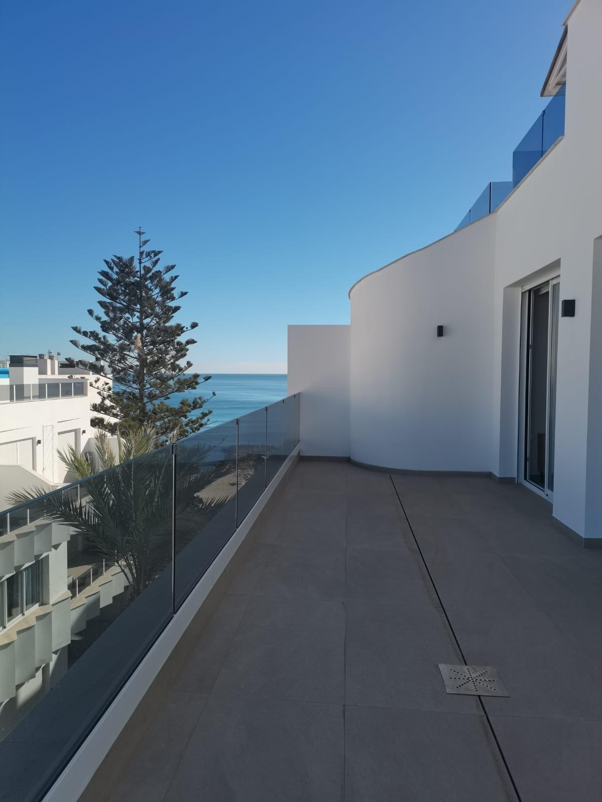 White modern balcony with glass railing, calm sea and clear blue sky beyond the terrace edge.