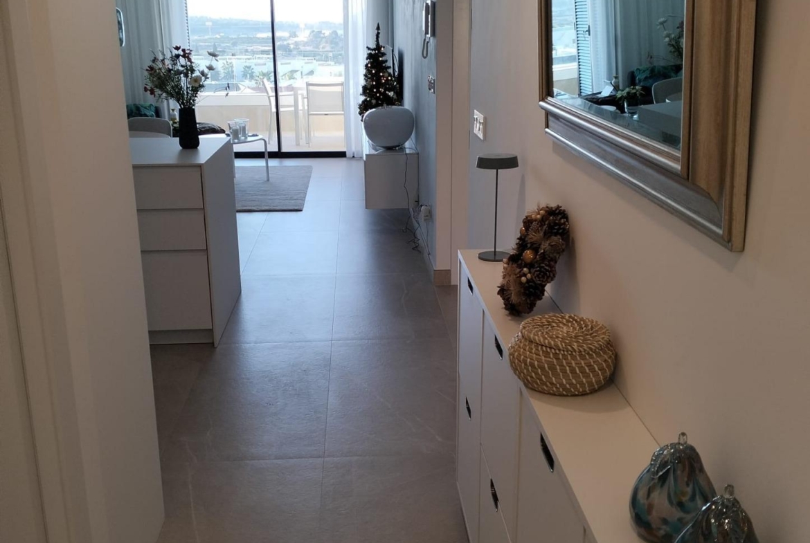Bright hallway with white cabinets on the right, decorative baskets, a large mirror, and a balcony door showing an outdoor view.