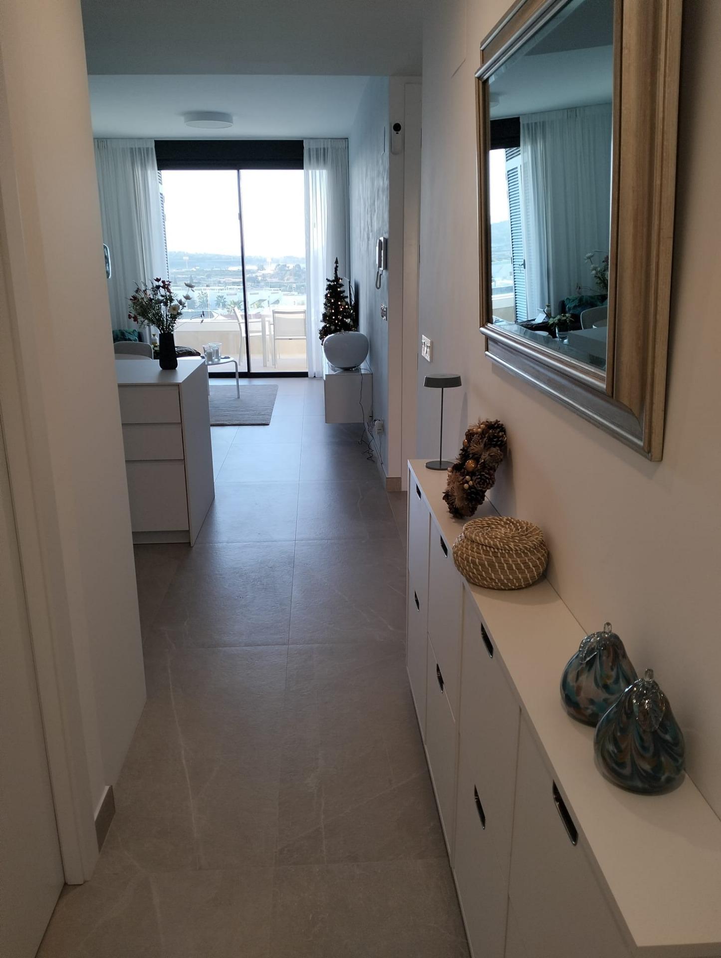 Bright hallway with white cabinets on the right, decorative baskets, a large mirror, and a balcony door showing an outdoor view.