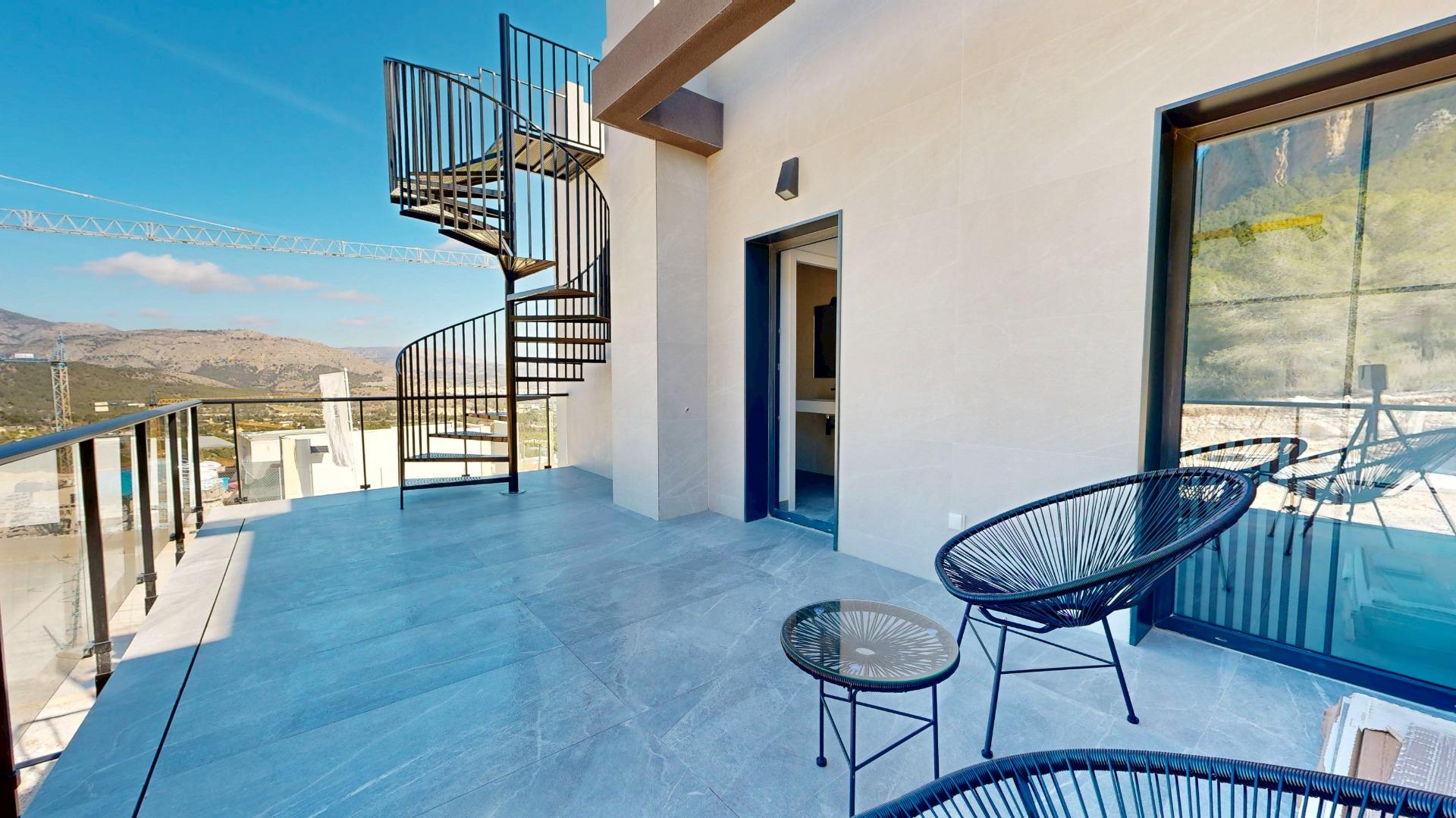 Modern balcony with glass railing, blue tiled floor, and a black spiral staircase overlooking mountains.