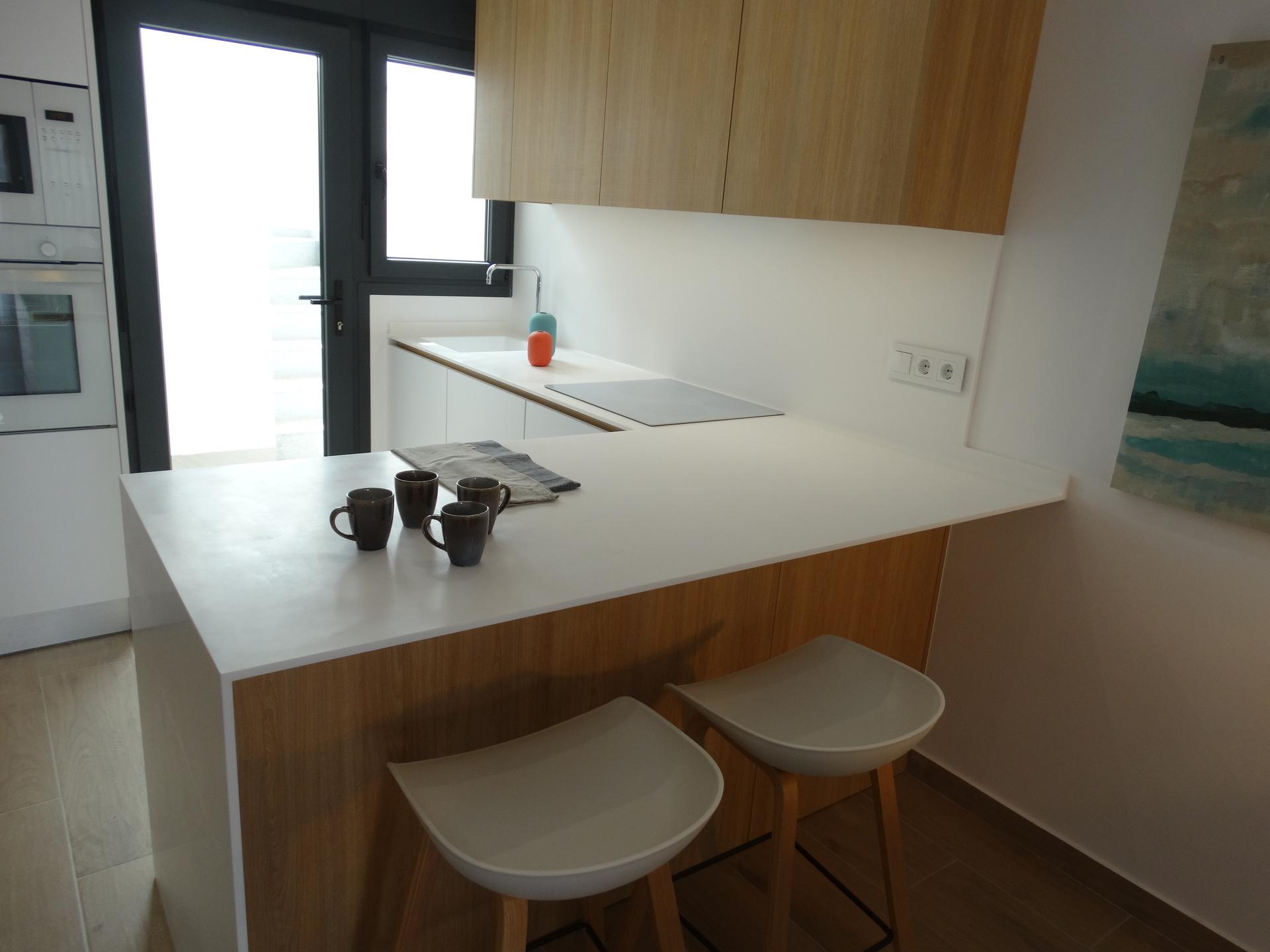 Contemporary kitchen with a white island, wood base cabinets, two white bar stools, and five dark mugs on the counter.