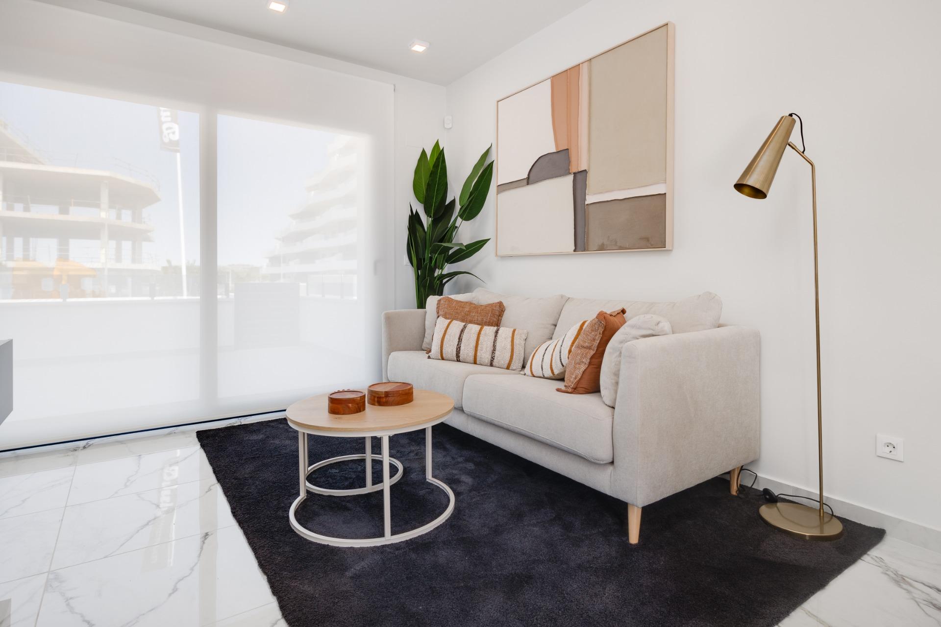 Bright living room with a beige sofa, abstract wall art, tall gold floor lamp, plant, and round coffee table on a dark rug.