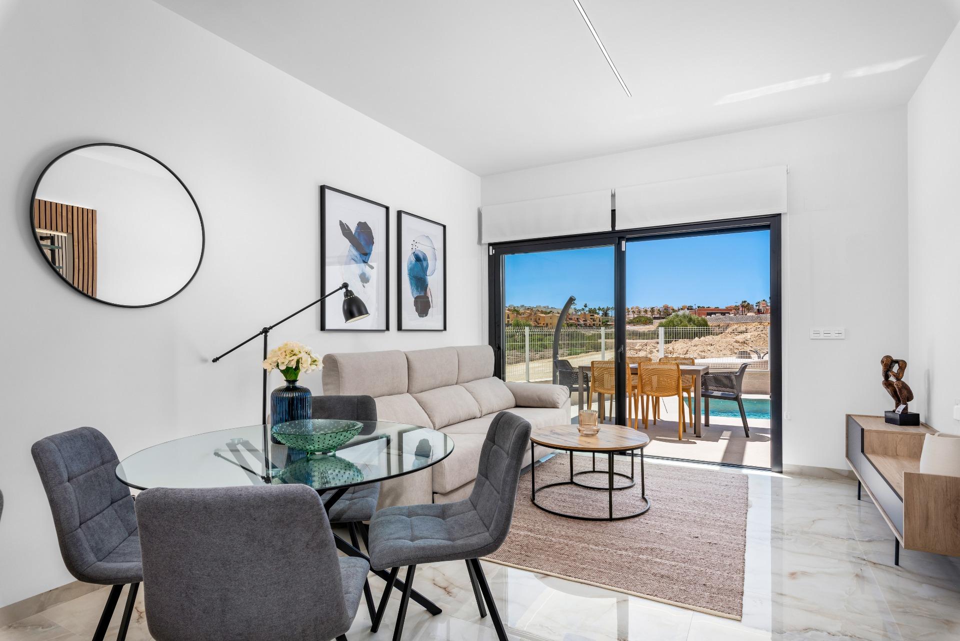 Bright living area with a glass dining table, gray chairs, and a beige sofa, leading to an outdoor patio through sliding doors.