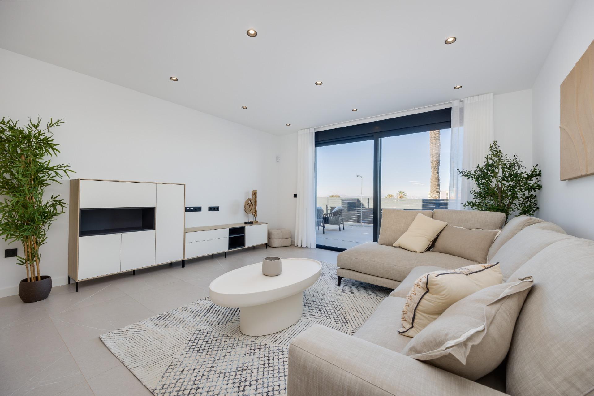 Bright modern living room with a beige sectional, white storage units, and a sliding glass door to a balcony.