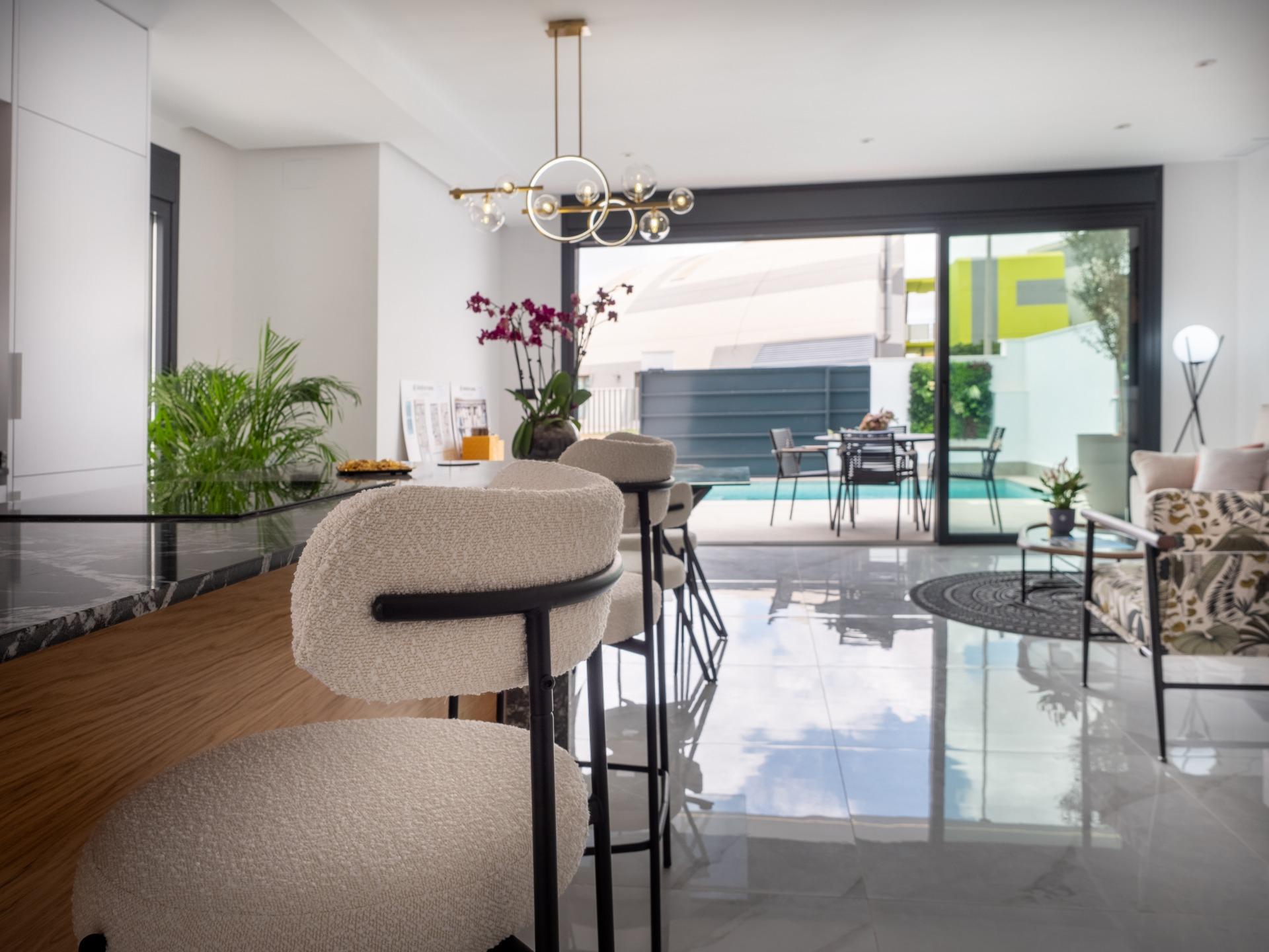 Open living area with a marble-topped bar and cream boucle stools facing large glass doors to an outdoor pool area.