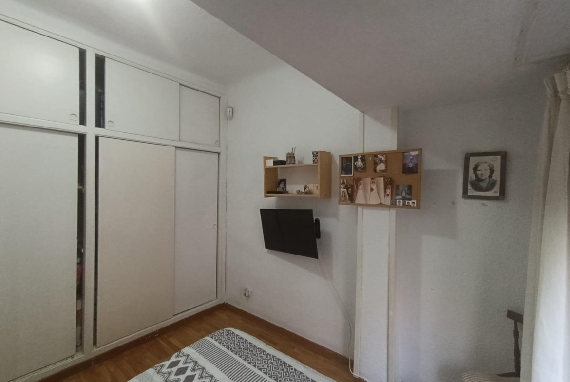 Bedroom with white built-in wardrobes on the left, a wall-mounted TV in the middle, and photo boards on the wall above.