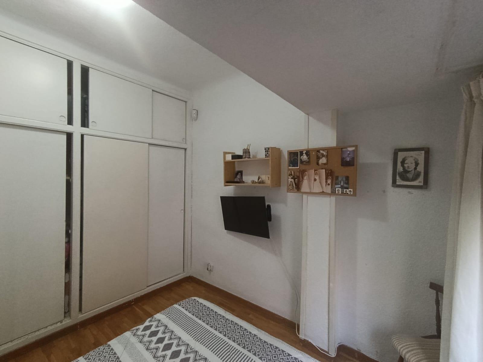 Bedroom with white built-in wardrobes on the left, a wall-mounted TV in the middle, and photo boards on the wall above.