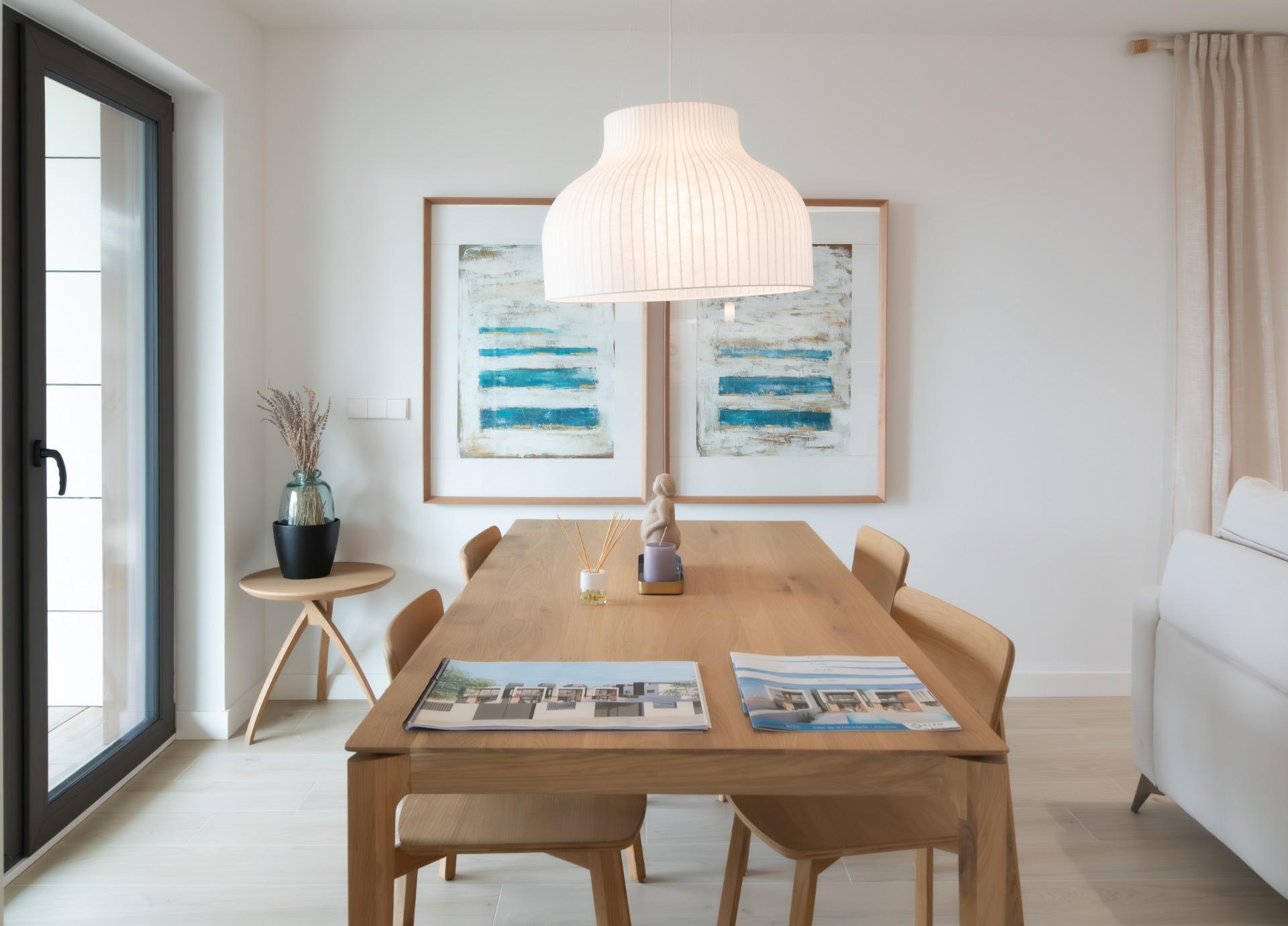Bright dining room with a wooden table and chairs, a white pendant lamp, and abstract blue artwork on the wall behind.